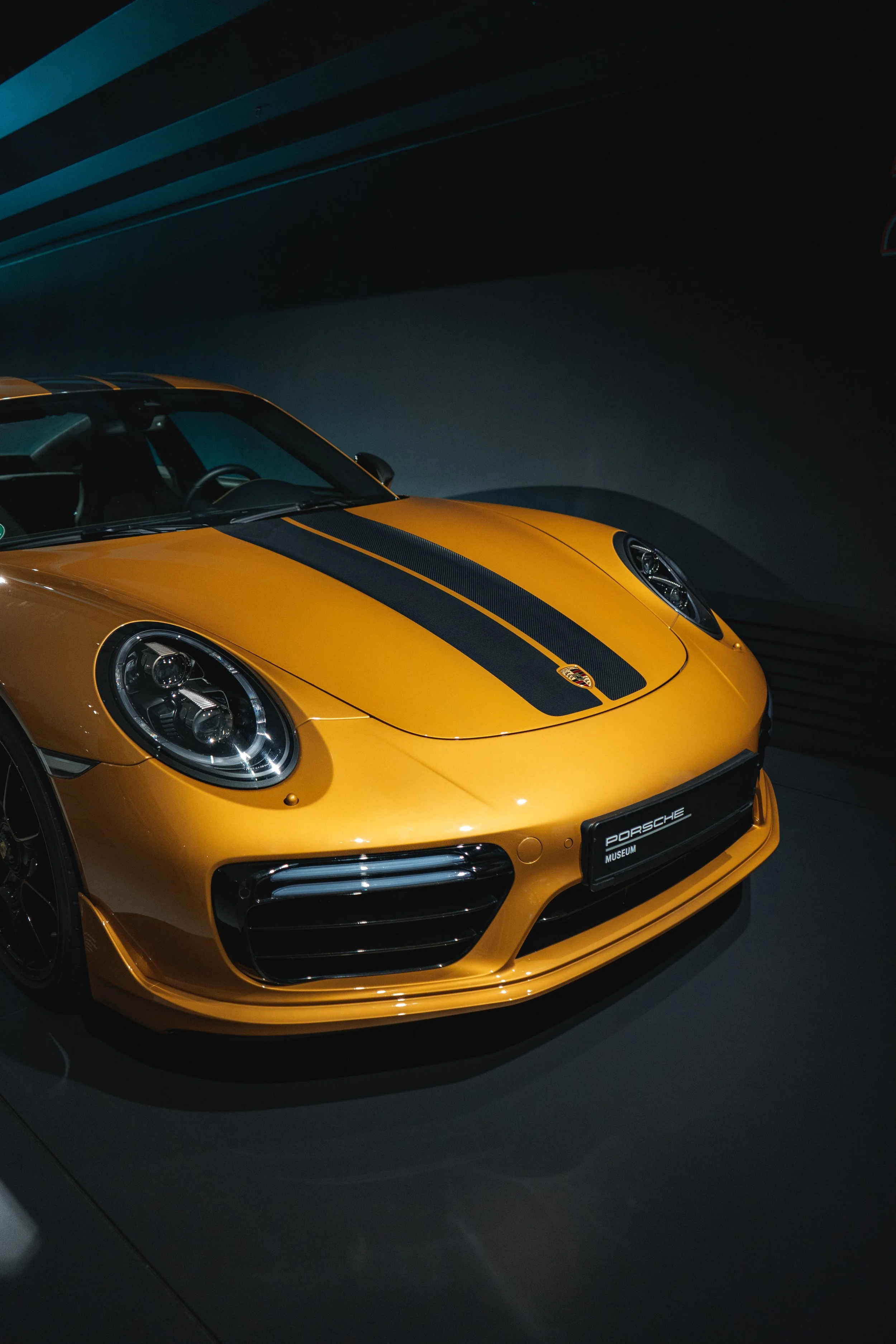 Yellow Porsche sports car with a black stripe on the hood, displayed at a Porsche museum.