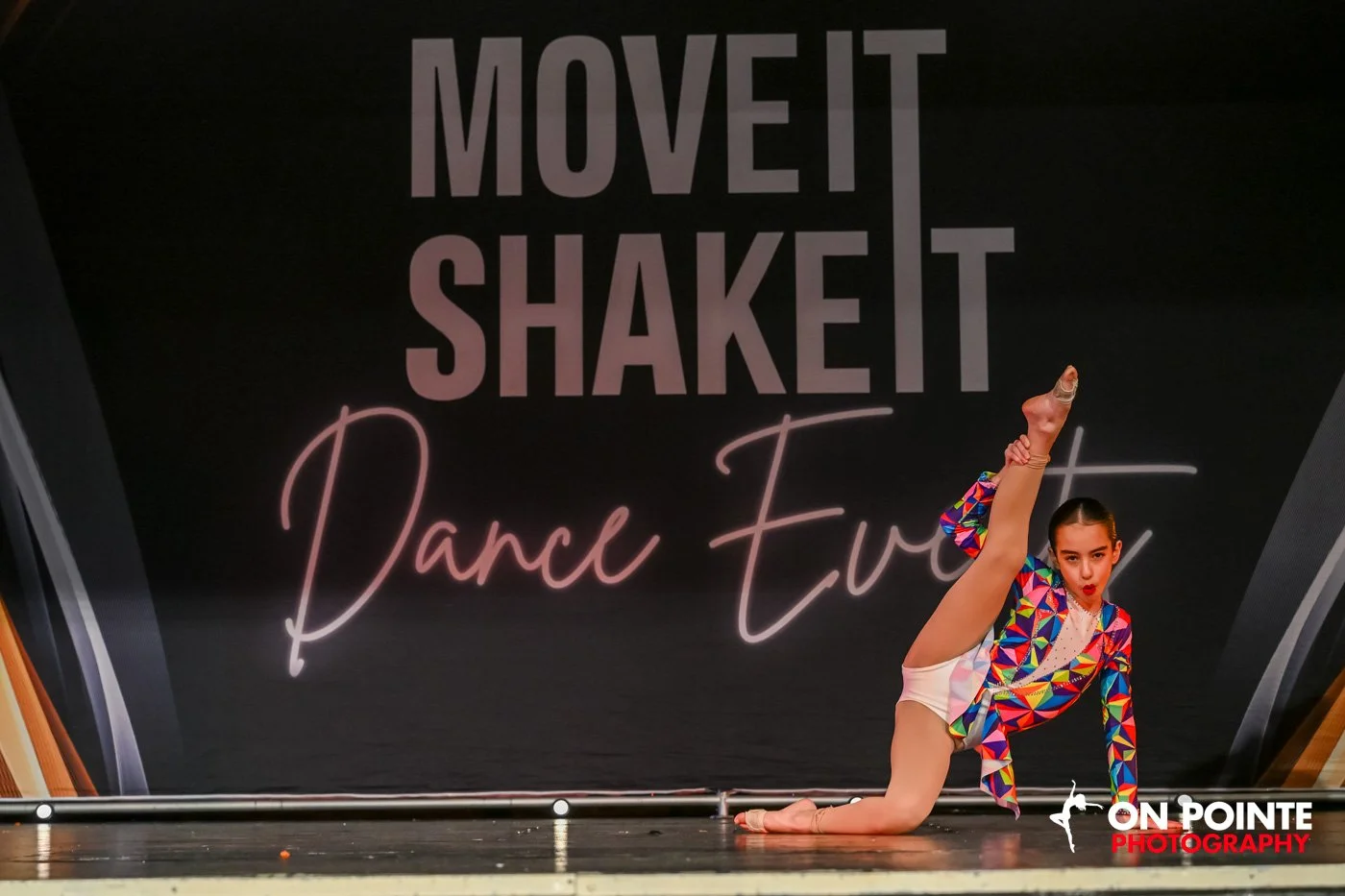 Dancer performing on stage during a dance competition, wearing a colorful costume and holding one leg up.