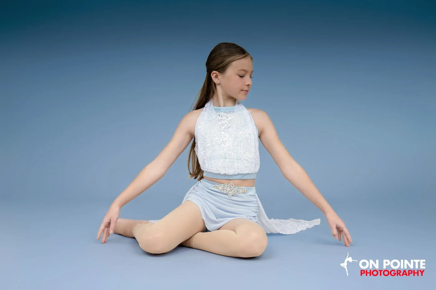 Young girl in a blue dance costume sitting on a blue background.
