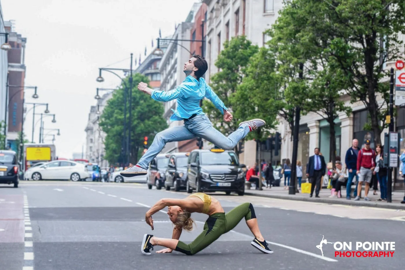 Man jumping in the air over a woman bending backwards in a street.