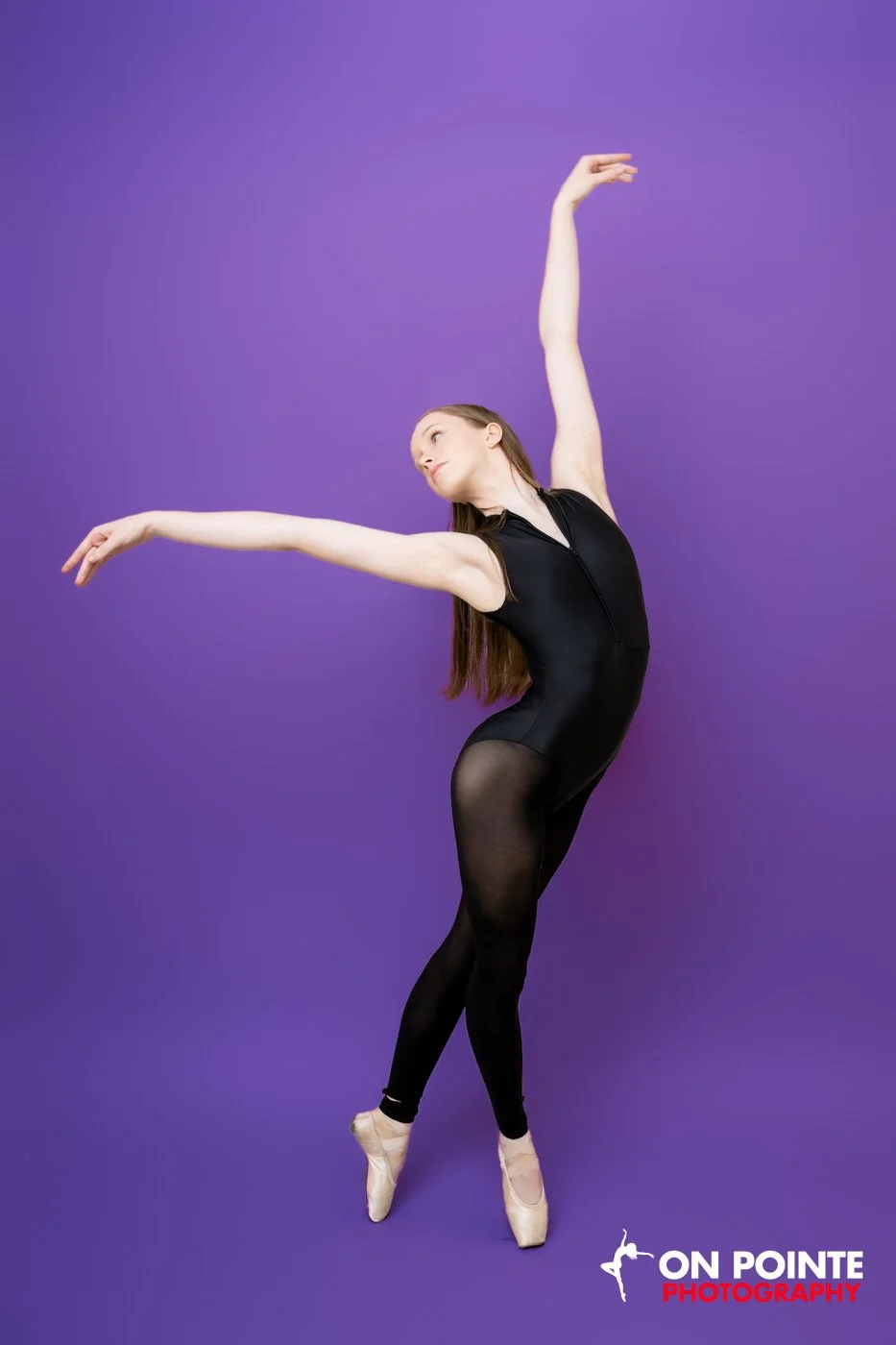 Ballet dancer posing in black leotard against purple background.
