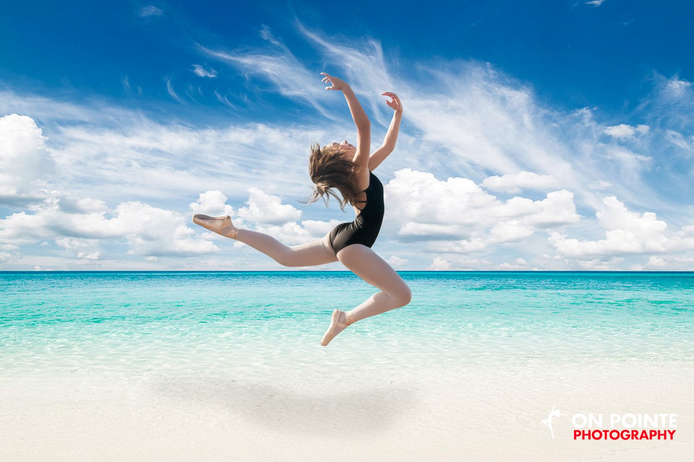 Dancer leaping on a beach in a black leotard with blue sky and ocean.