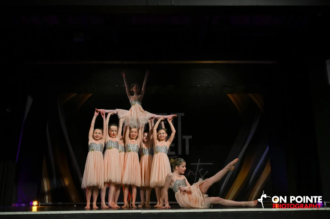 Group of young dancers in sequin and peach dresses performing on stage