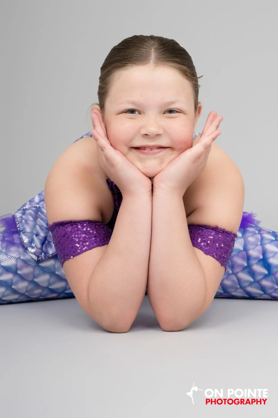 Child in a purple dance costume smiling and resting on hands.