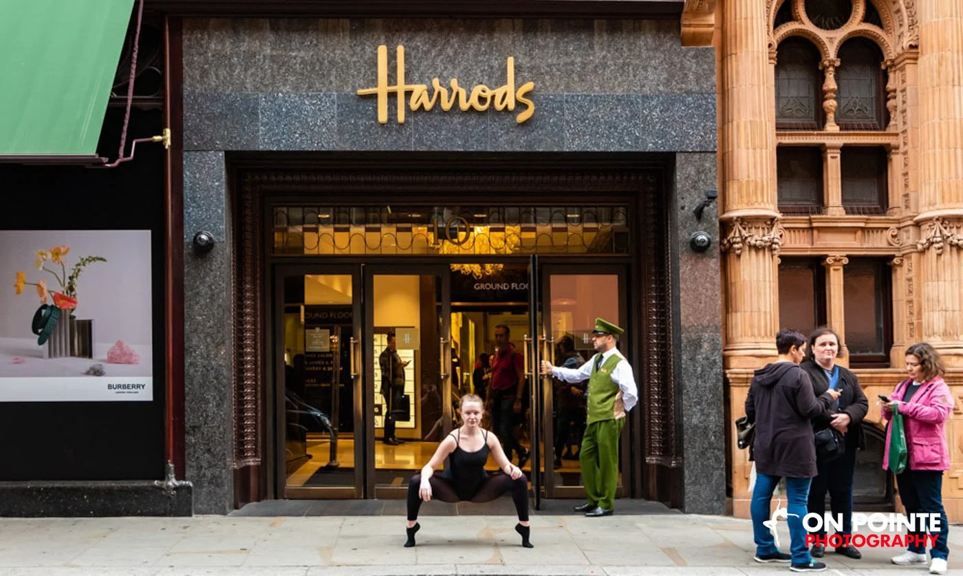 Dancer posing in front of Harrods entrance with people around.