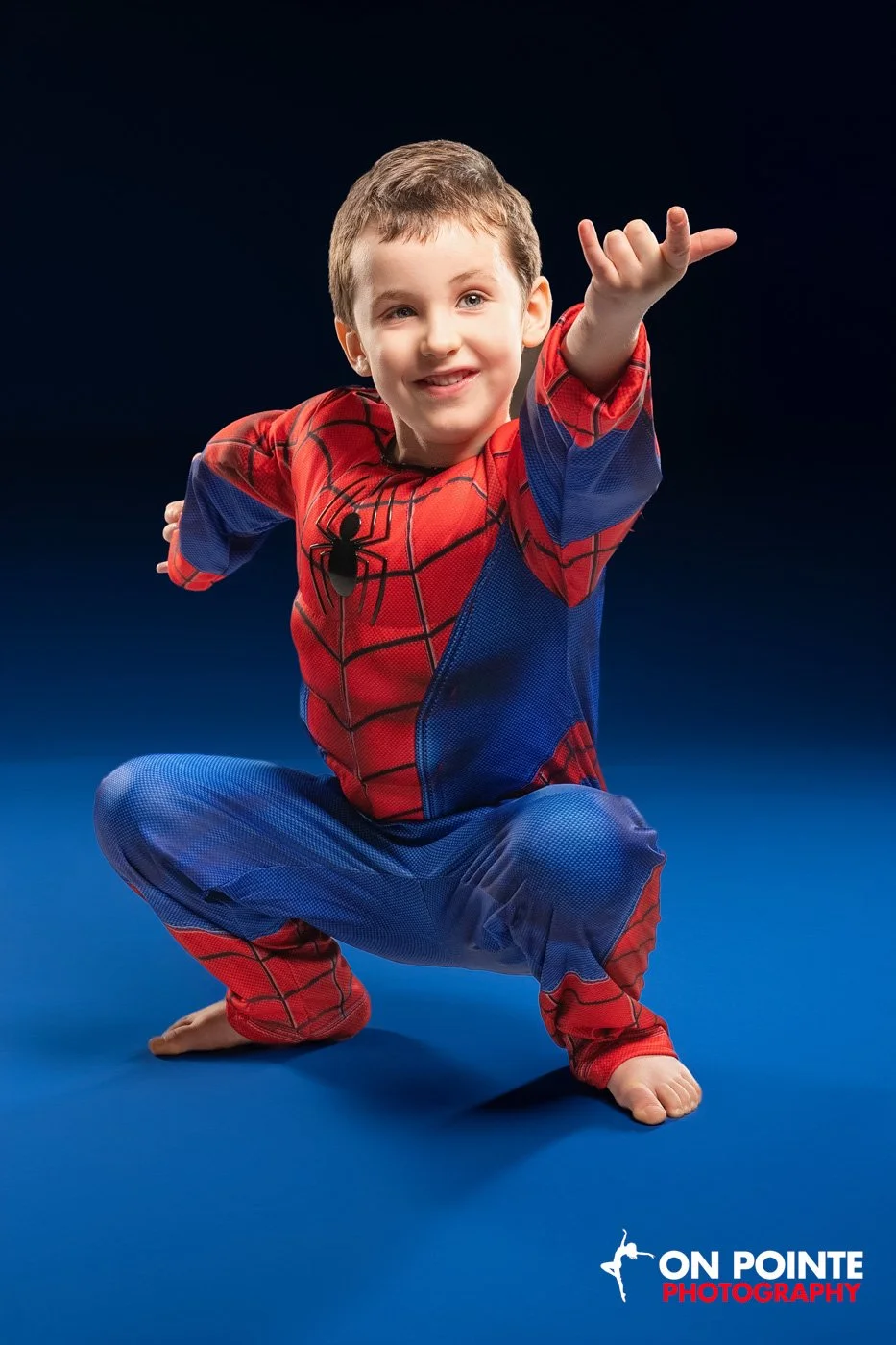 Child dressed in a Spider-Man costume striking a pose on a blue background.