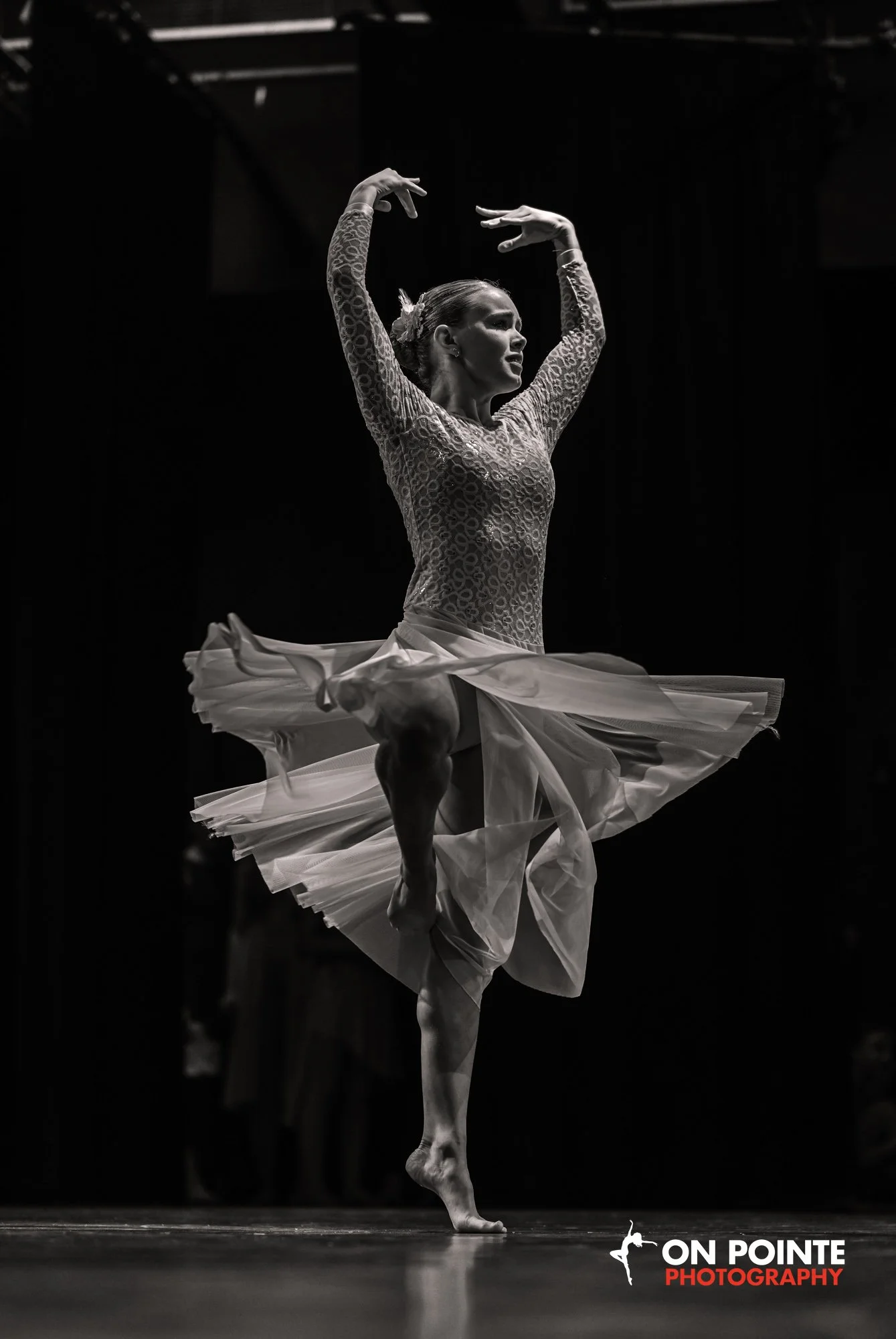 A ballerina performing on stage, captured mid-dance with a flowing dress, in black and white.