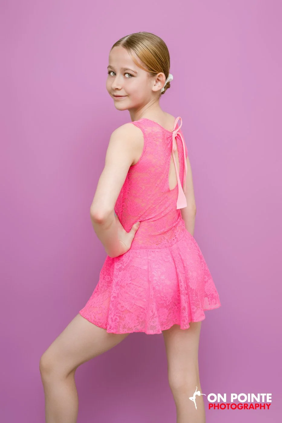Girl in a pink lace dress posing against a purple background.