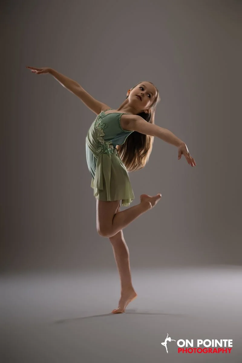 Young girl performing a ballet dance pose in a studio against a plain background.