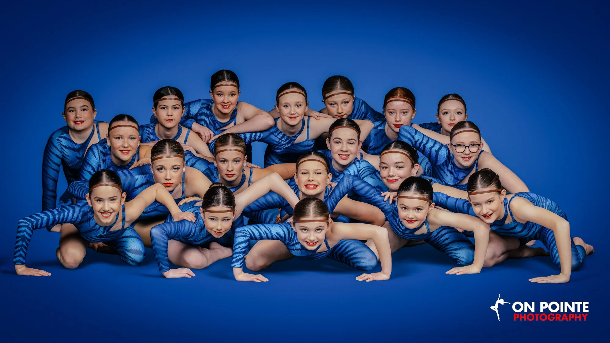 Group of young female gymnasts in matching blue costumes posing on a blue background