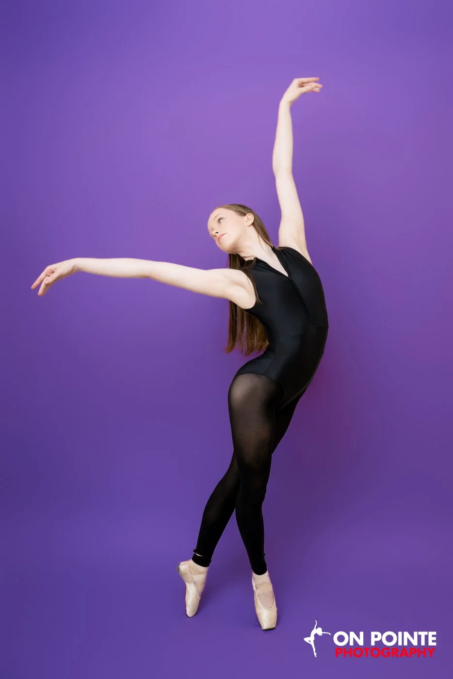 Ballet dancer in black leotard and tights performing a pose against a purple background, with 'On Pointe Photography' logo in bottom right corner.