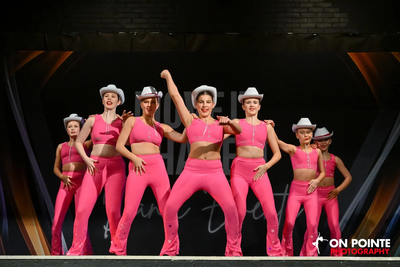 Group of dancers in pink costumes and white cowboy hats performing on stage