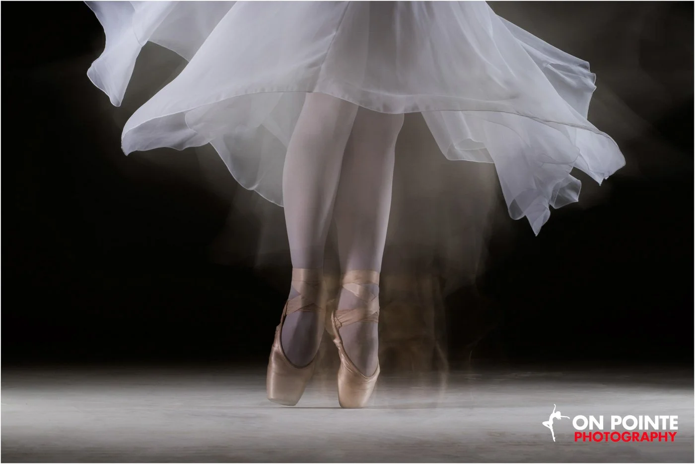 Ballerina on pointe, wearing a white flowing dress and ballet slippers.