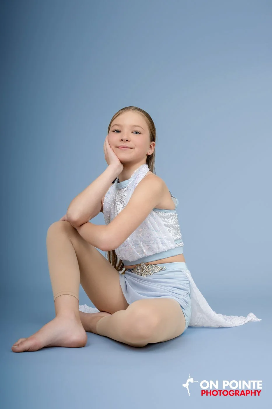 Young girl in a dance costume poses confidently against a blue background.