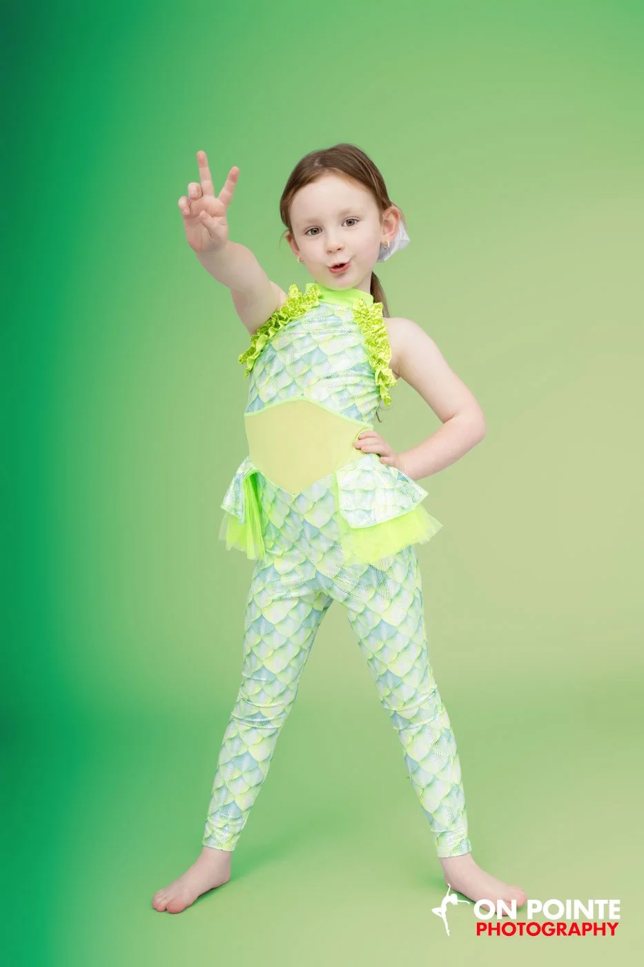 Child posing in green costume with peace sign on green background.