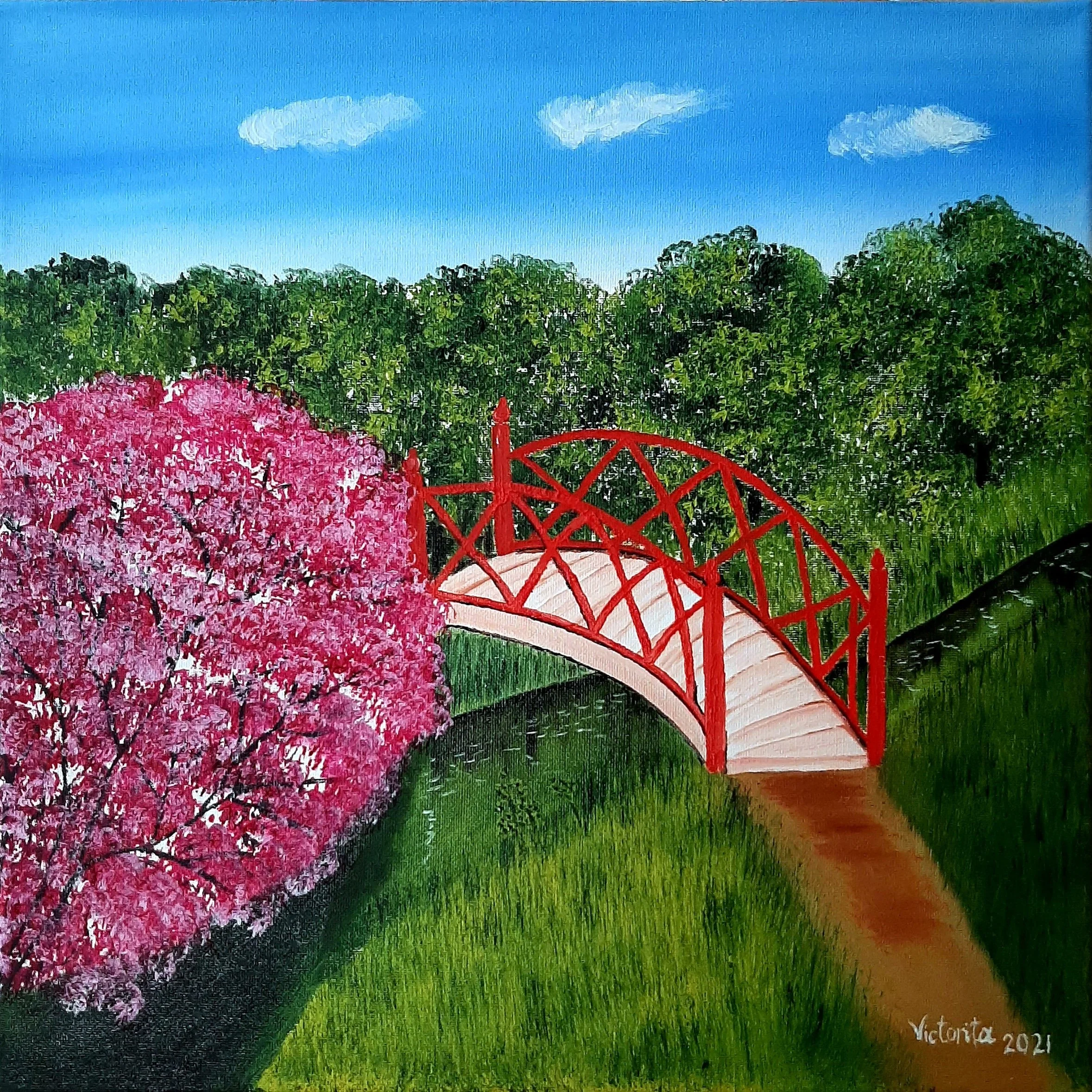 A landscape painting featuring a pink flowering tree, a red wooden bridge, green bushes, and a pathway leading into the distance, with clouds in a blue sky. The painting is signed "Victoria 2021" in the bottom right corner.