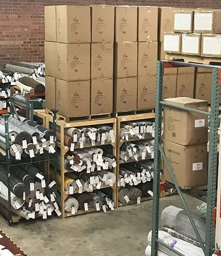 End-to-End Fulfillment Solutions. Warehouse storage with stacked boxes on shelves and coiled industrial hoses or pipes on metal racks.