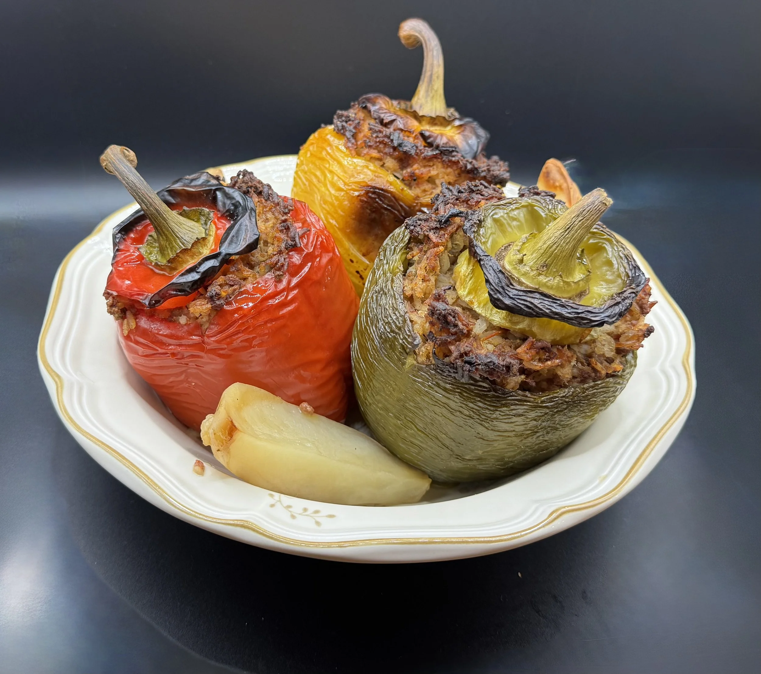 Three stuffed bell peppers—red, yellow, and green—on a white plate, garnished with cooked bacon bits, with a black background.