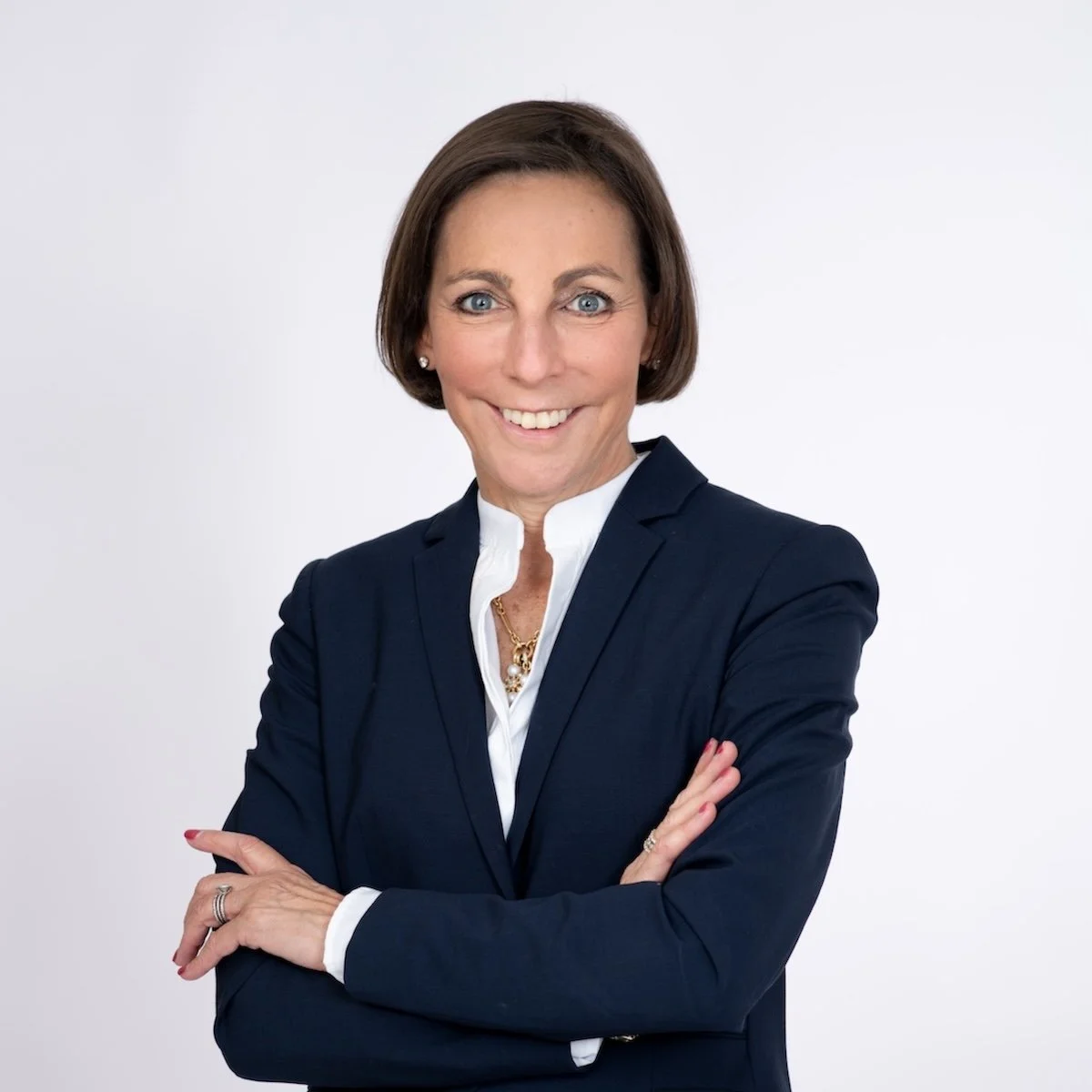 Headshot of Dr. Lisa Larkin smiling, arms crossed, wearing a navy blazer and white blouse against a light gray background.