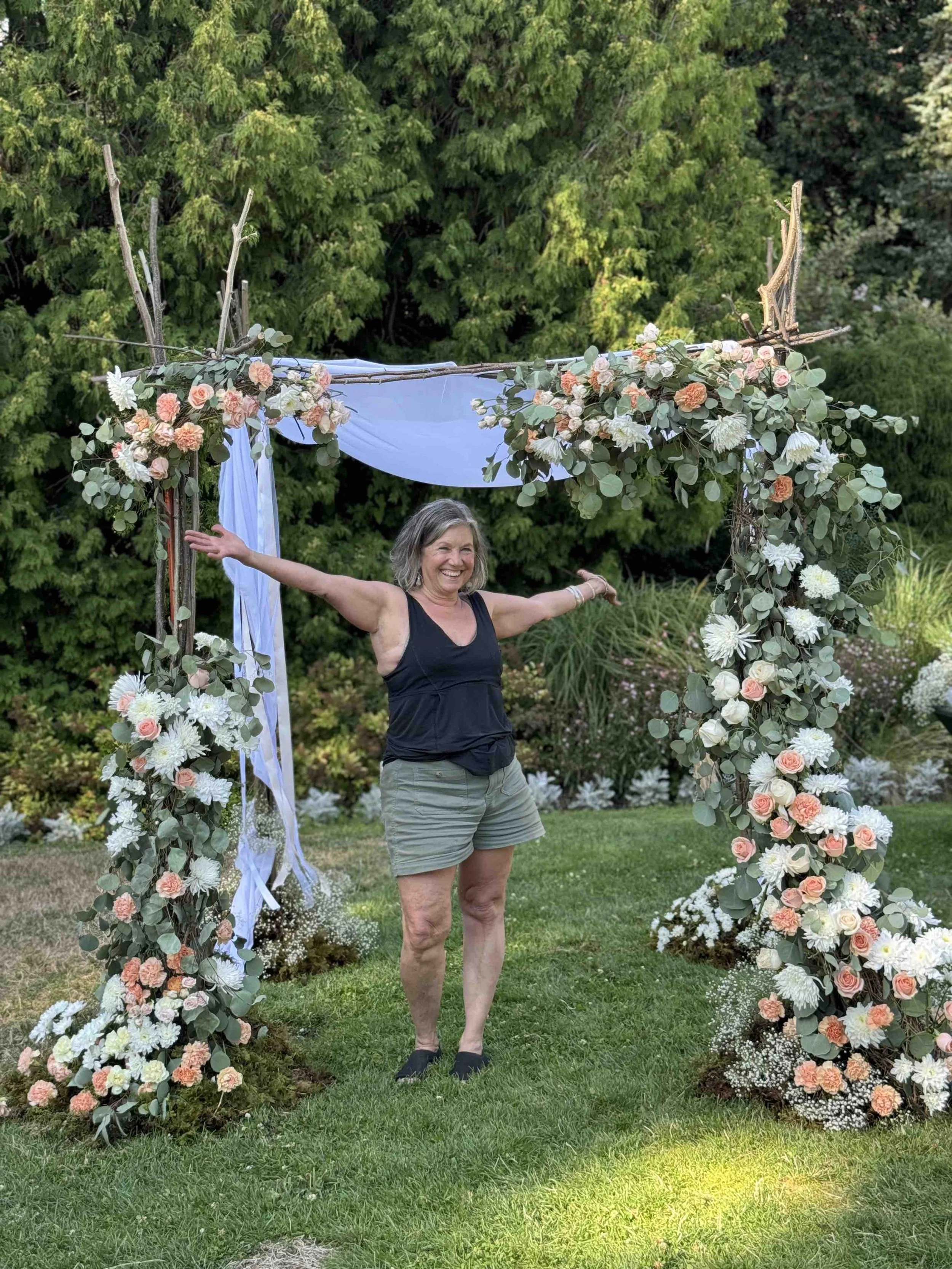Anne spreading arms under flower arch white smiling