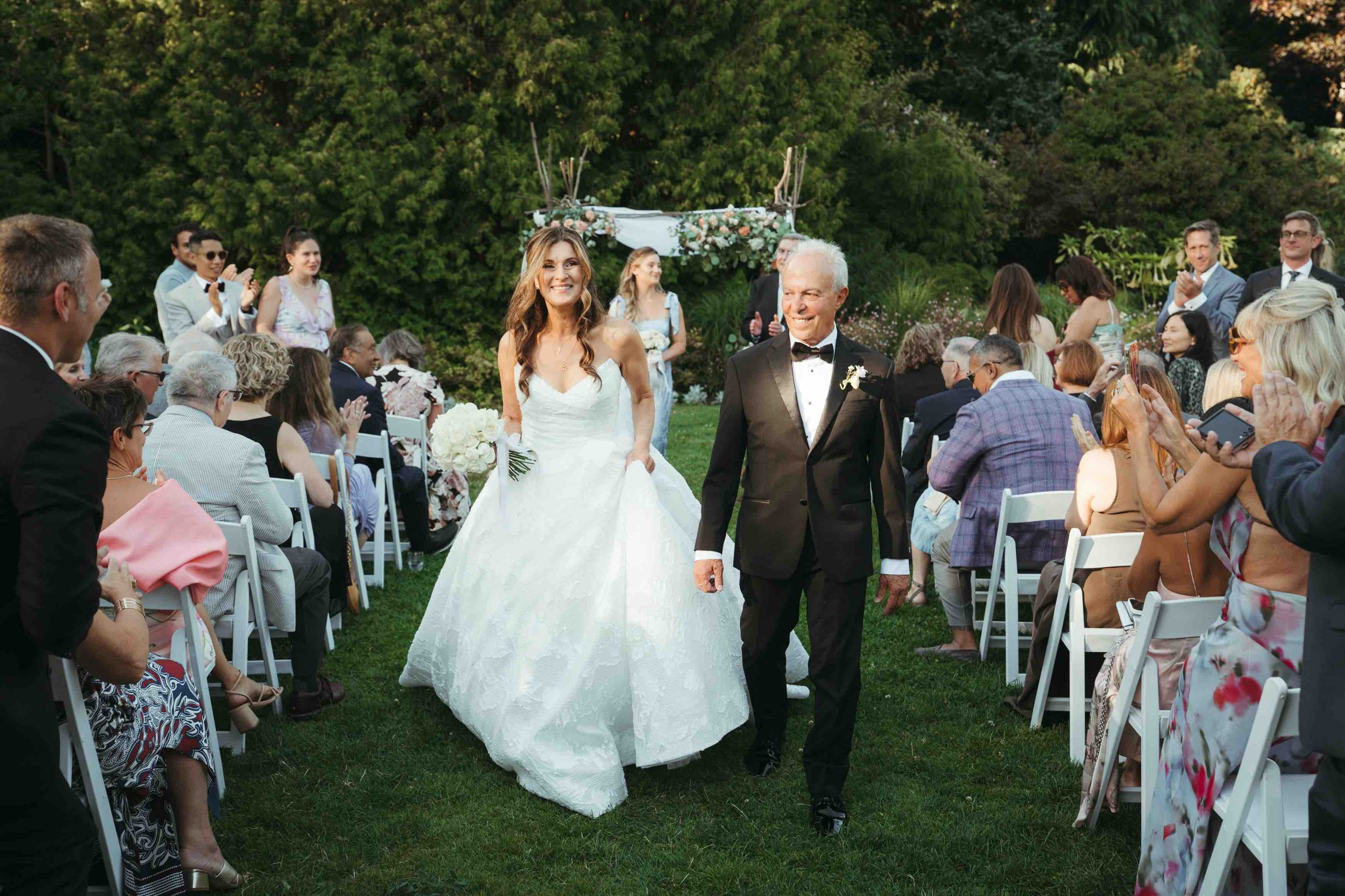 Bride and groom walking on grass with guests sitting
