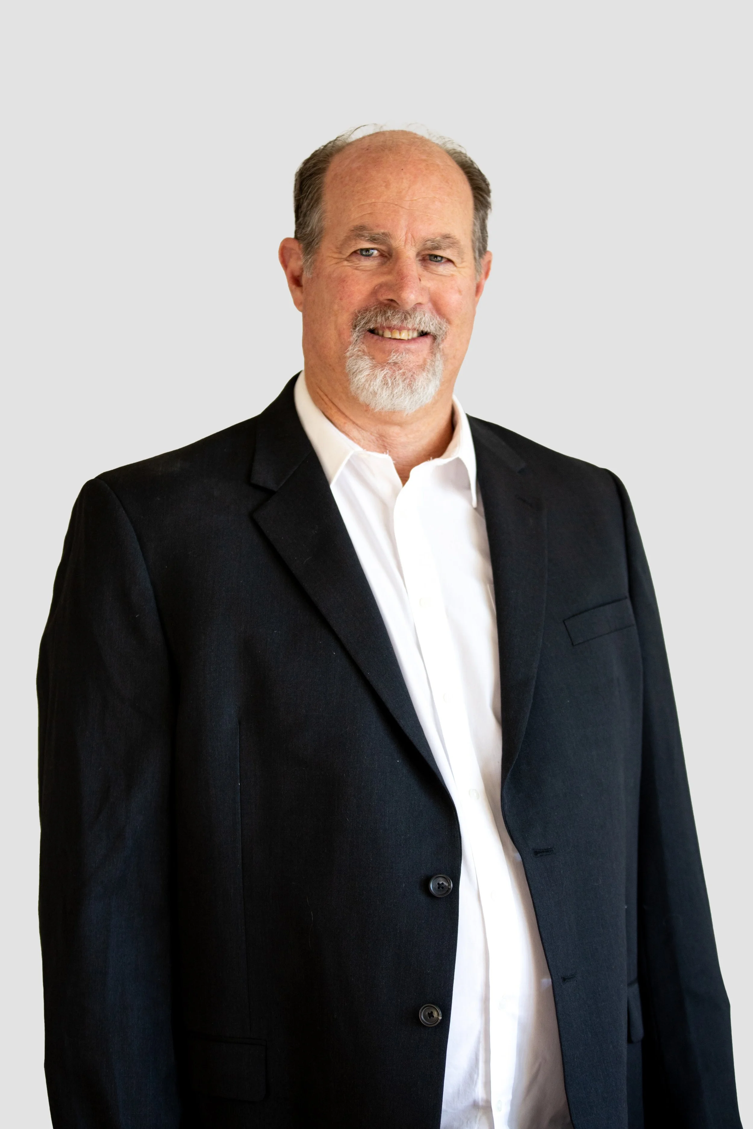 Chuck Lambert wearing a black suit jacket over a white dress shirt, standing against a plain light background.
