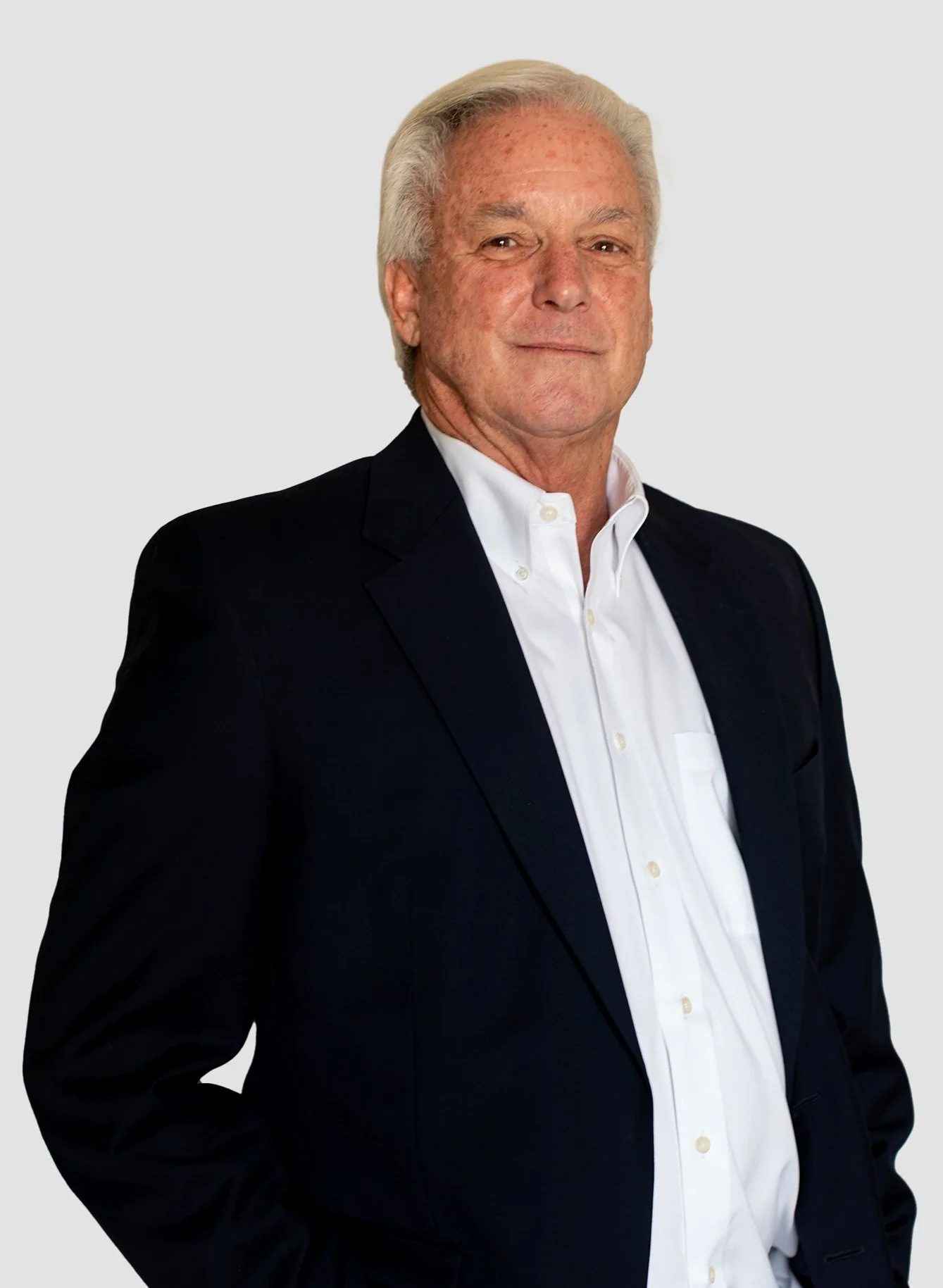Jimmy Johnston with gray hair wearing a dark suit and white shirt, standing against a light gray background.