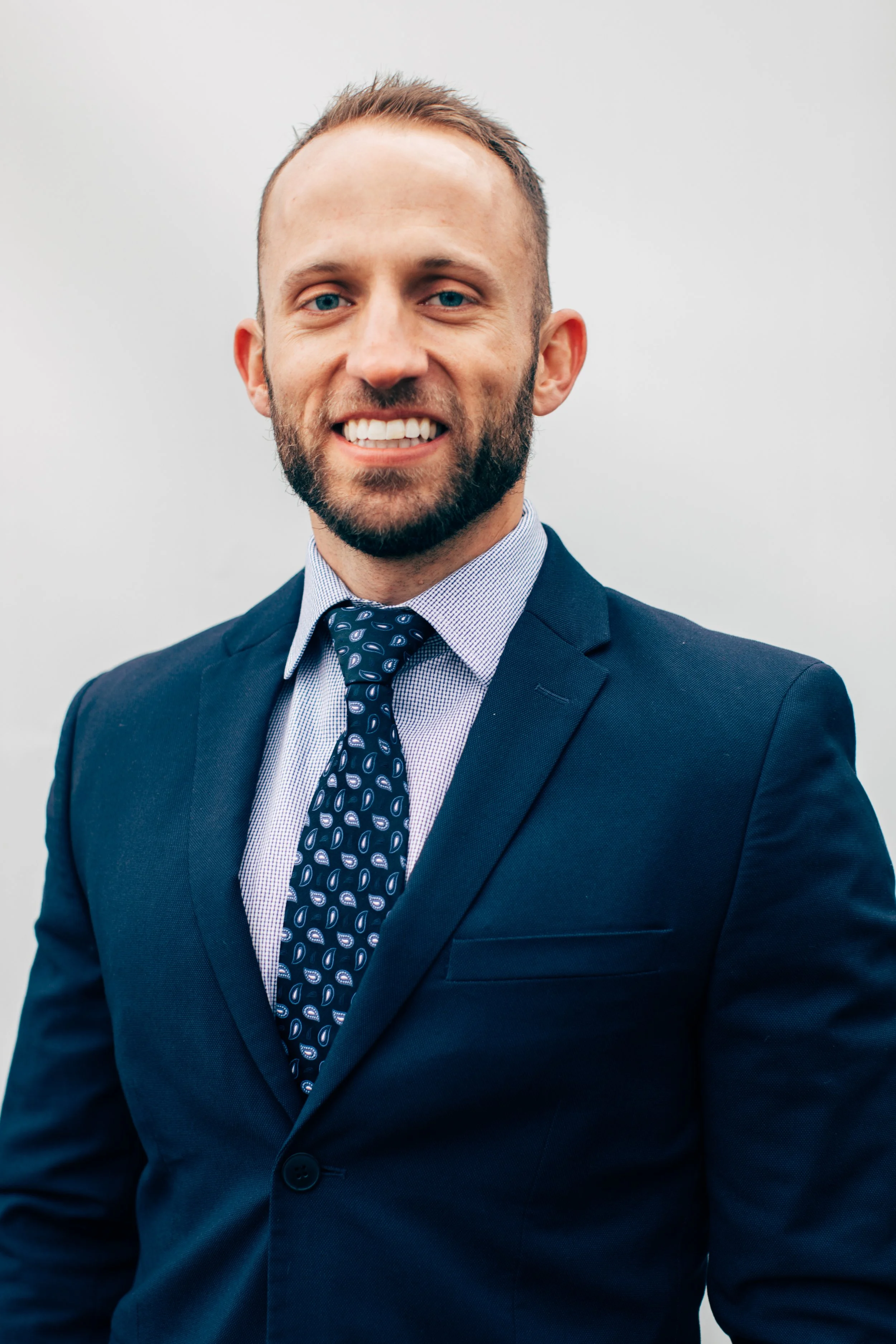 Freddy Ellis in a navy suit, light dress shirt, and patterned tie on a plain white background.