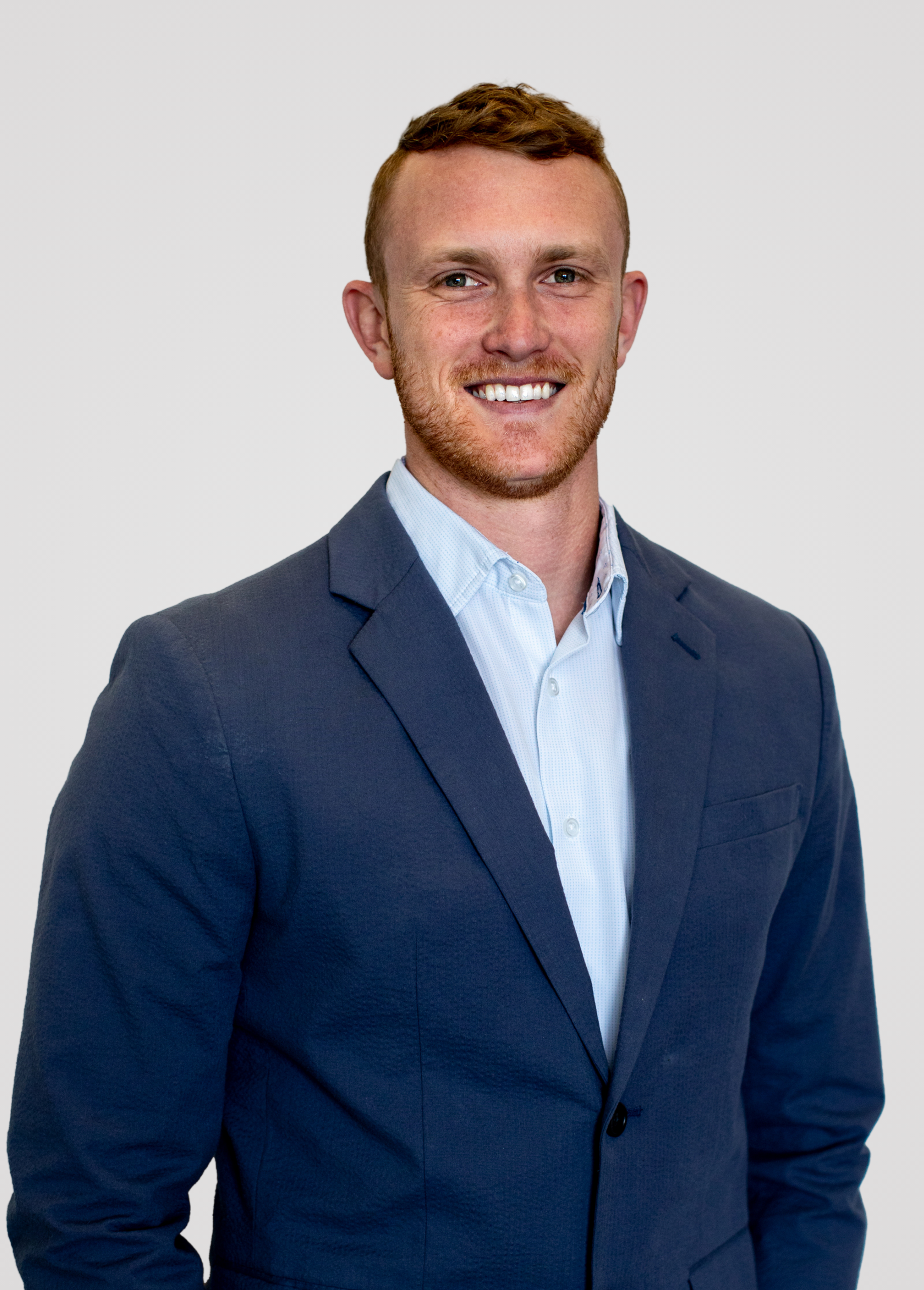 Kyle Nelson wearing a navy blue suit and light blue shirt, standing against a plain white background.
