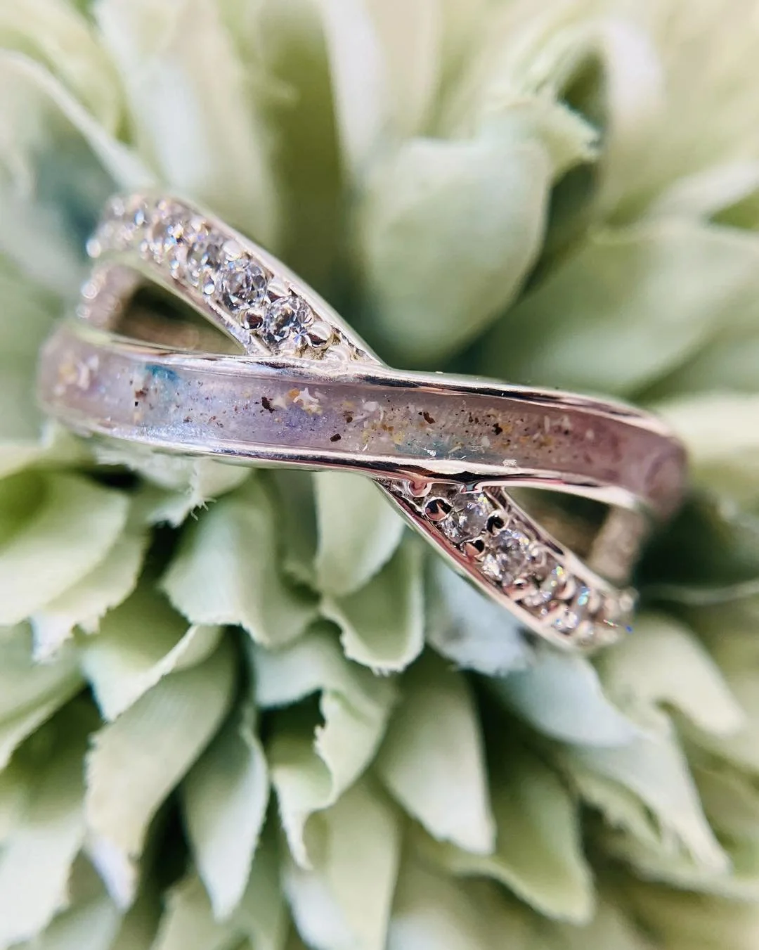 Close-up of intertwined silver rings with embedded small diamonds, resting on green leaves.