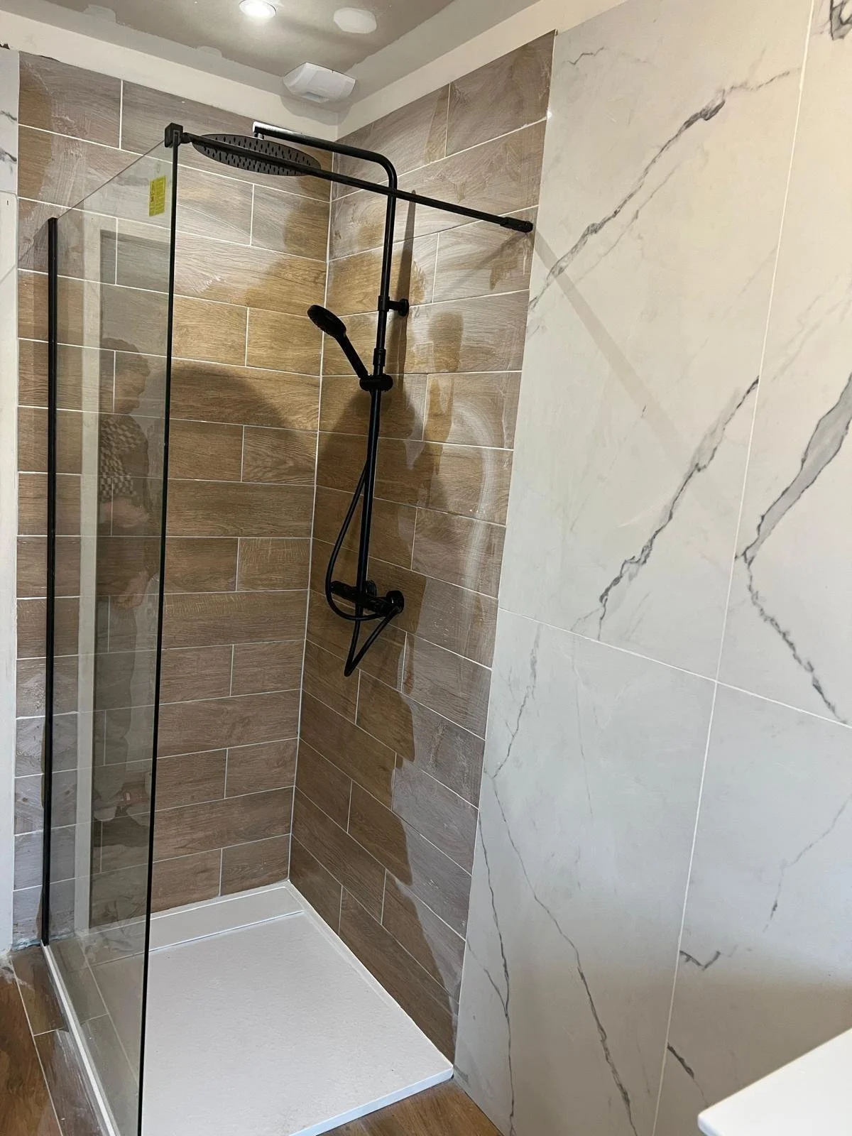 Douche moderne avec paroi en verre, receveur blanc, murs carrelés en bois clair et marbre blanc avec veines grises.