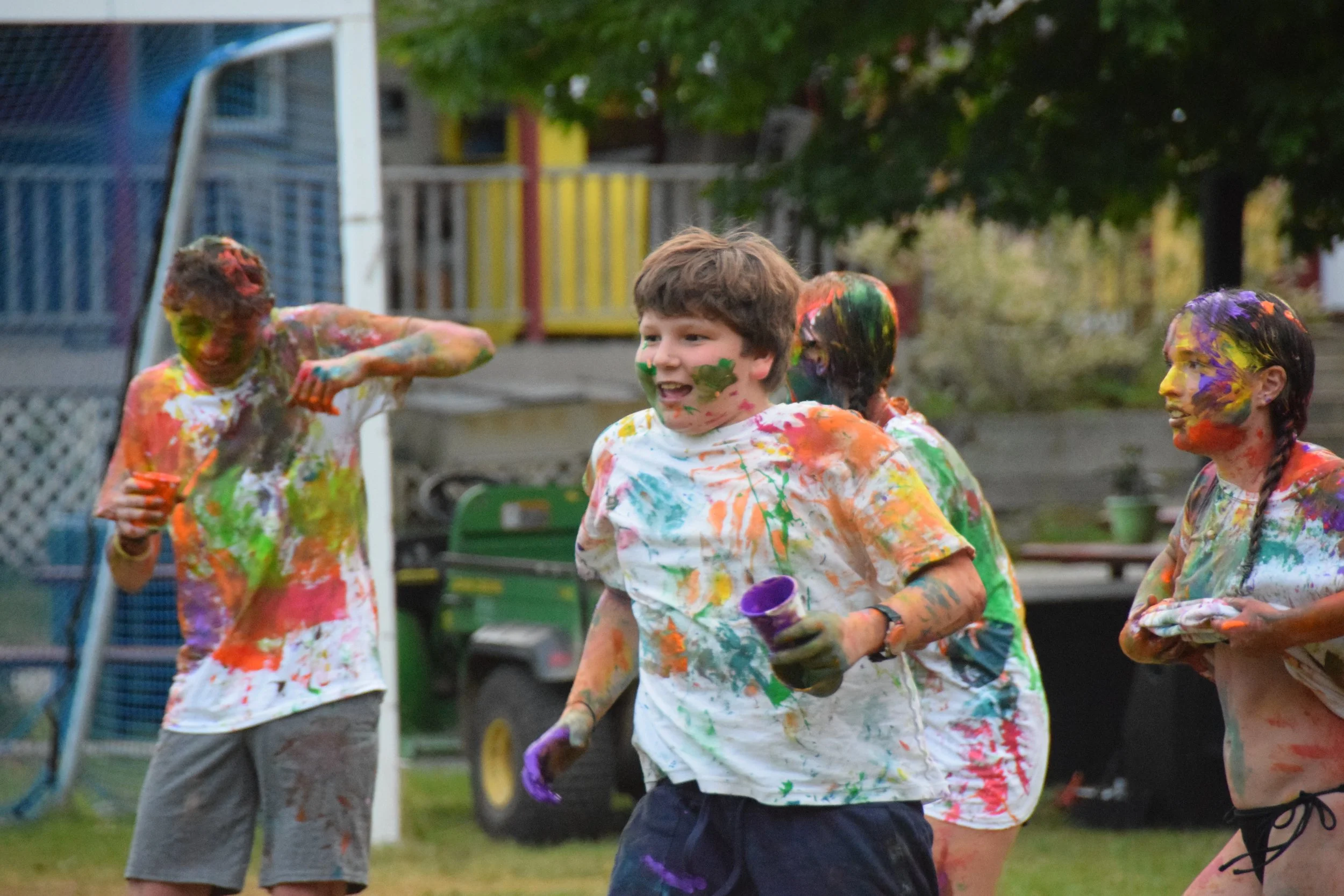 Group of children playing with colored powder outdoors, smiling and covered in paint.