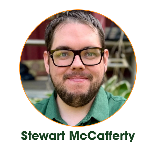 Portrait of a man with glasses and a beard wearing a green shirt, smiling in front of a blurred background.