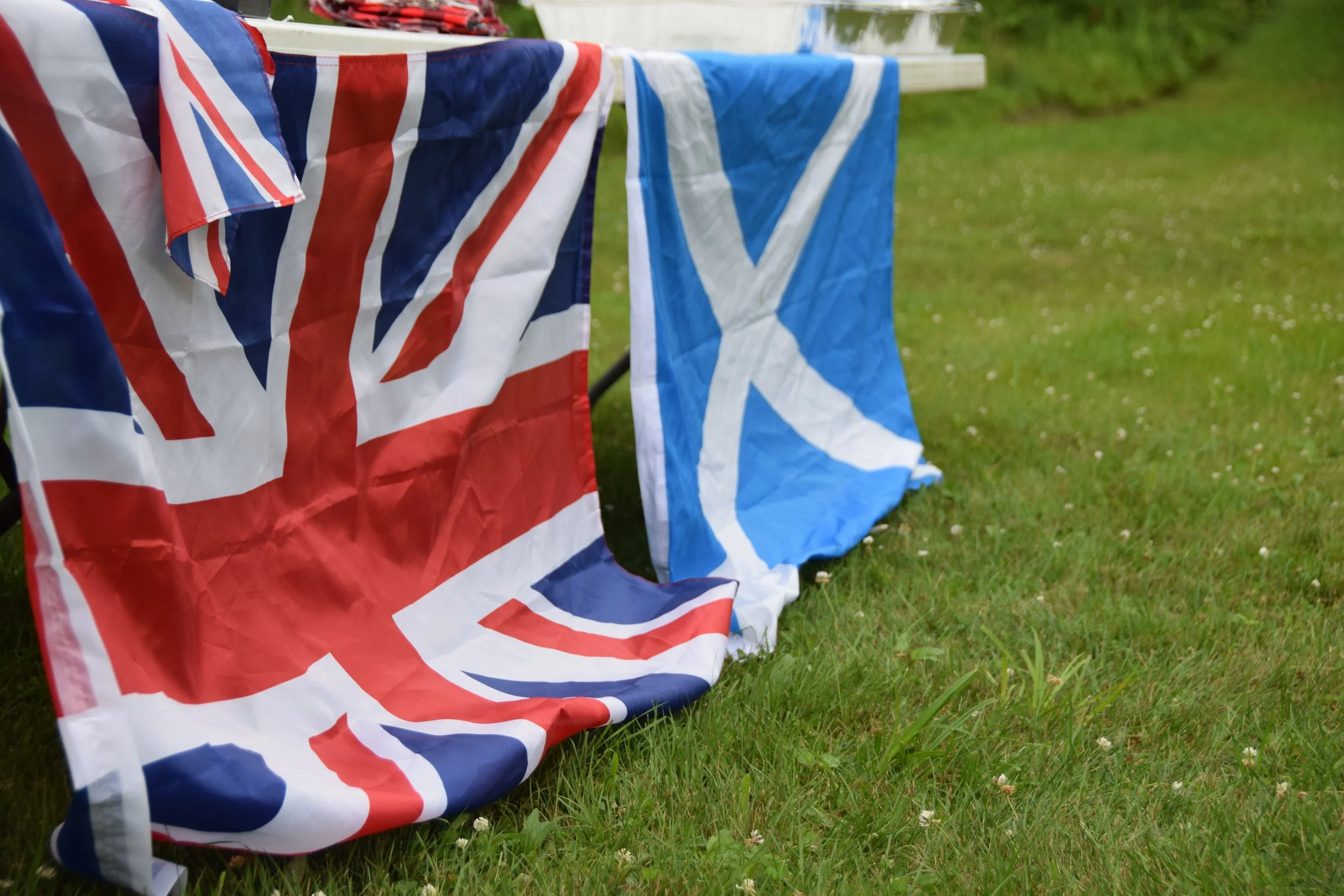 Two flags, one of the United Kingdom (Union Jack) and one of Scotland, hanging on a clothesline outdoors on a grassy area.