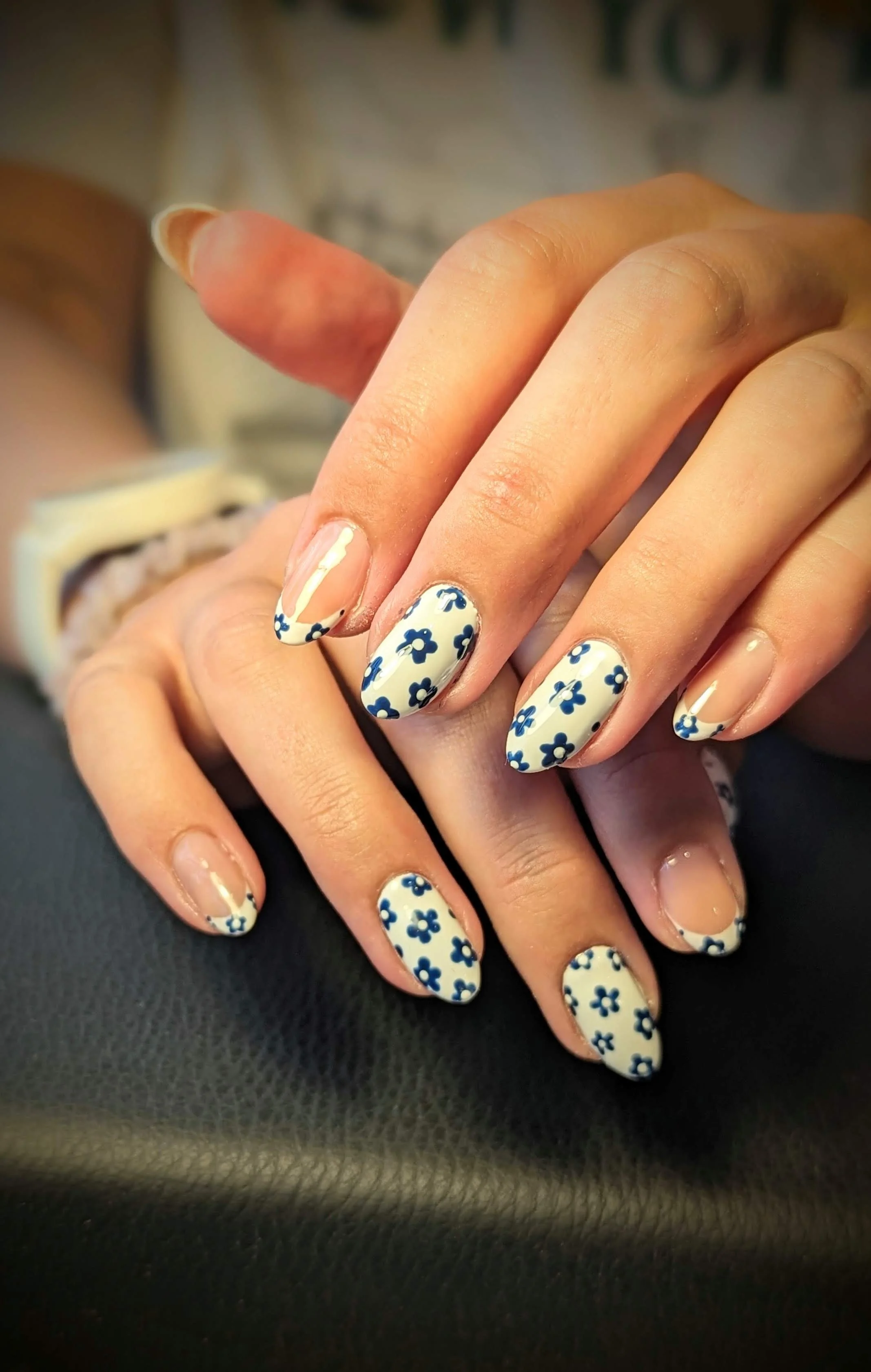 Hands with builder gel nails featuring floral nail art, created by Row Cosmetic Tattoo & Beauty in Leeds (LS16 6AL). The nails are decorated with a white base and blue flower designs, giving a delicate and artistic finish