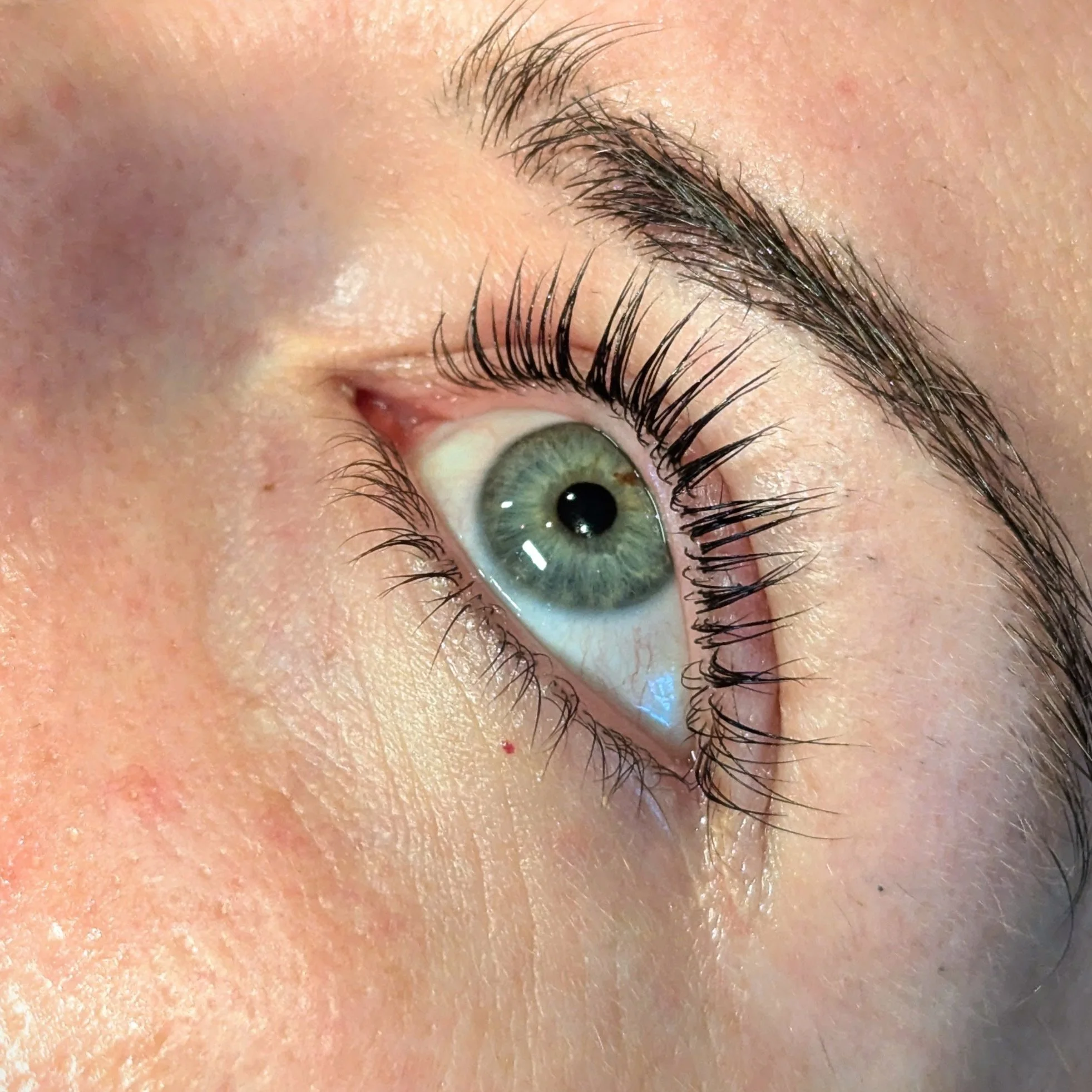 Close-up of a woman's eye showing lifted and curled lashes after a lash lift treatment at Row Cosmetic Tattoo & Beauty in Leeds (LS16 6AL). Her lashes appear long and defined, enhancing her bright green eye, while her brows are neatly shaped, adding