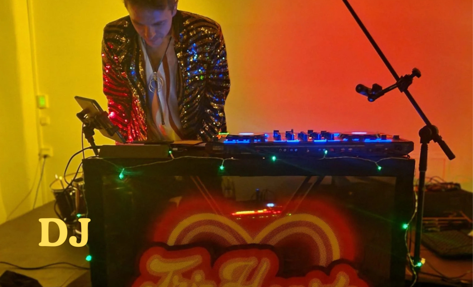 En DJ som spelar musik vid en DJ-utrustning med färgglada ljus och en mikrofon på en mikrofonstativ i ett rum med orange och gult väggfärger.