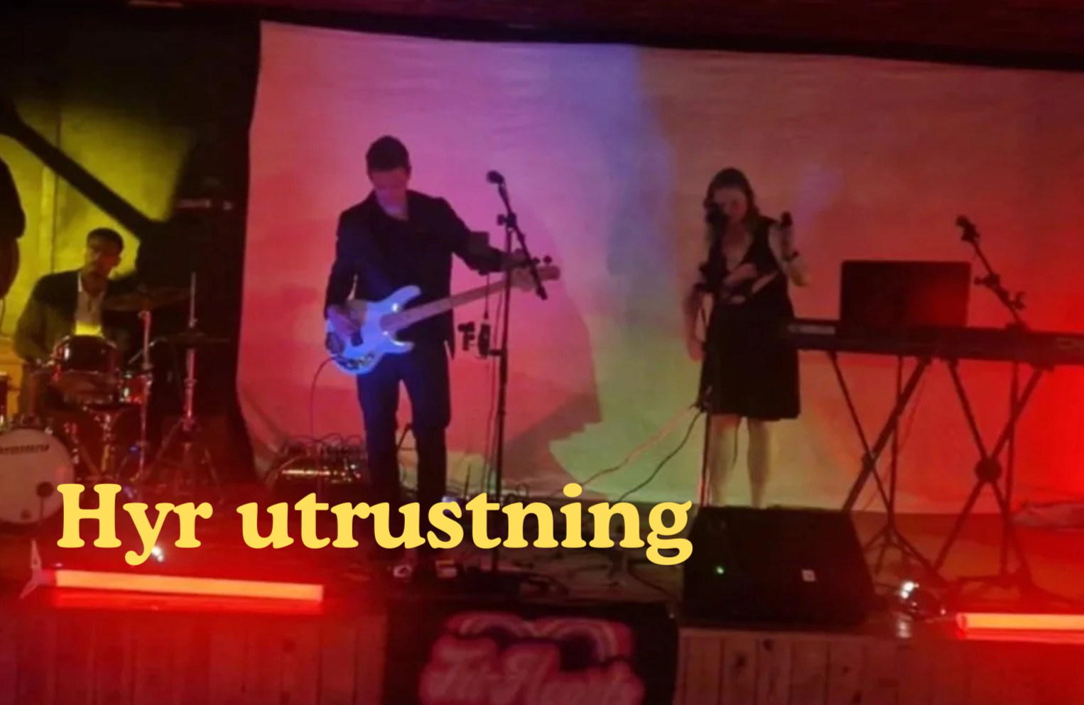 En levande musikgrupp med tre musiker på scen, en person som spelar gitarr, en som spelar trummor och en som sjunger, med färgglad scenbelysning och en text som säger "Hyr utrustning".