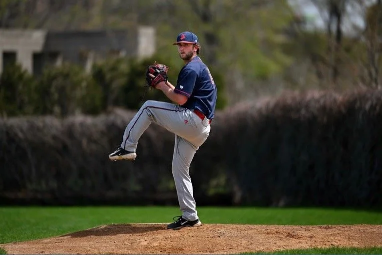 A baseball pitcher is in the middle of a pitch on the mound, wearing a blue jersey, gray pants, and a blue cap.