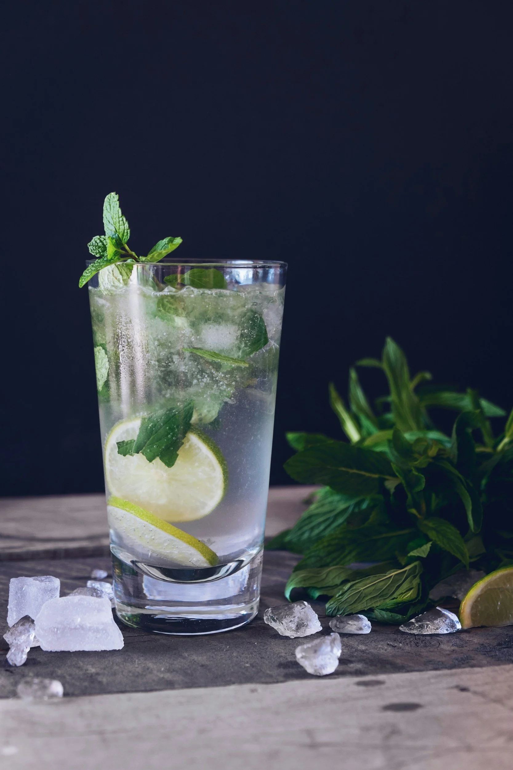 A glass of mojito with lime slices, mint leaves, and ice cubes on a wooden table.
