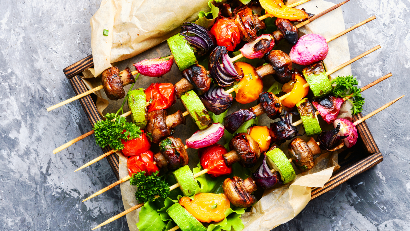 Assorted grilled vegetable skewers with zucchini, mushrooms, bell peppers, red onion, and cherry tomatoes on a parchment-lined tray.