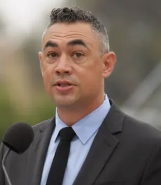 Man in suit and tie speaking at a microphone outdoors.