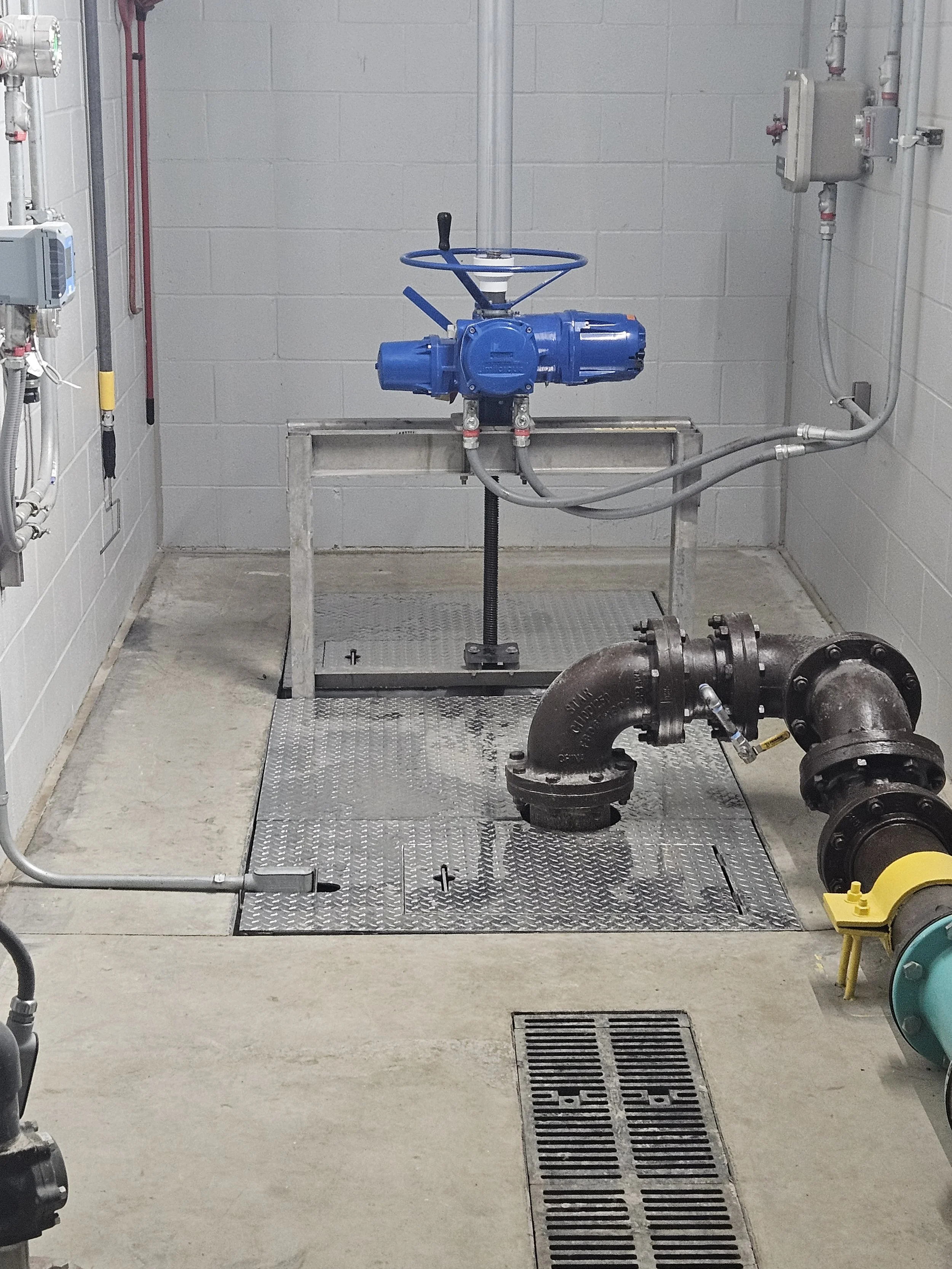 Industrial mechanical room with piping, valves, and a large blue valve actuator. custom floor with hatch doors.