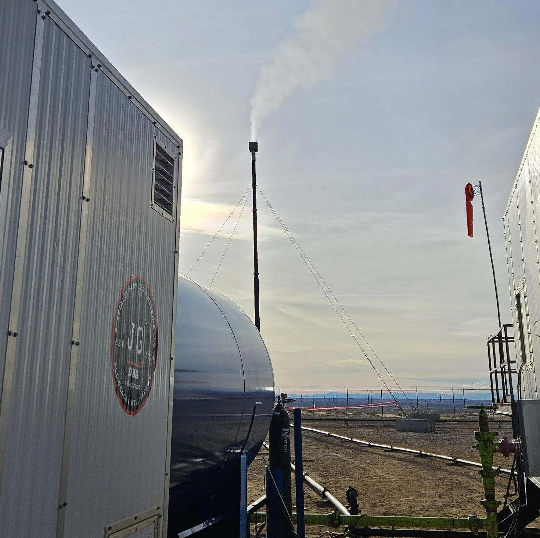 Oil storage tanks on a flat open land with a cloudy sky and mountains in the background. seperator for well testing and flowback, H2s gas