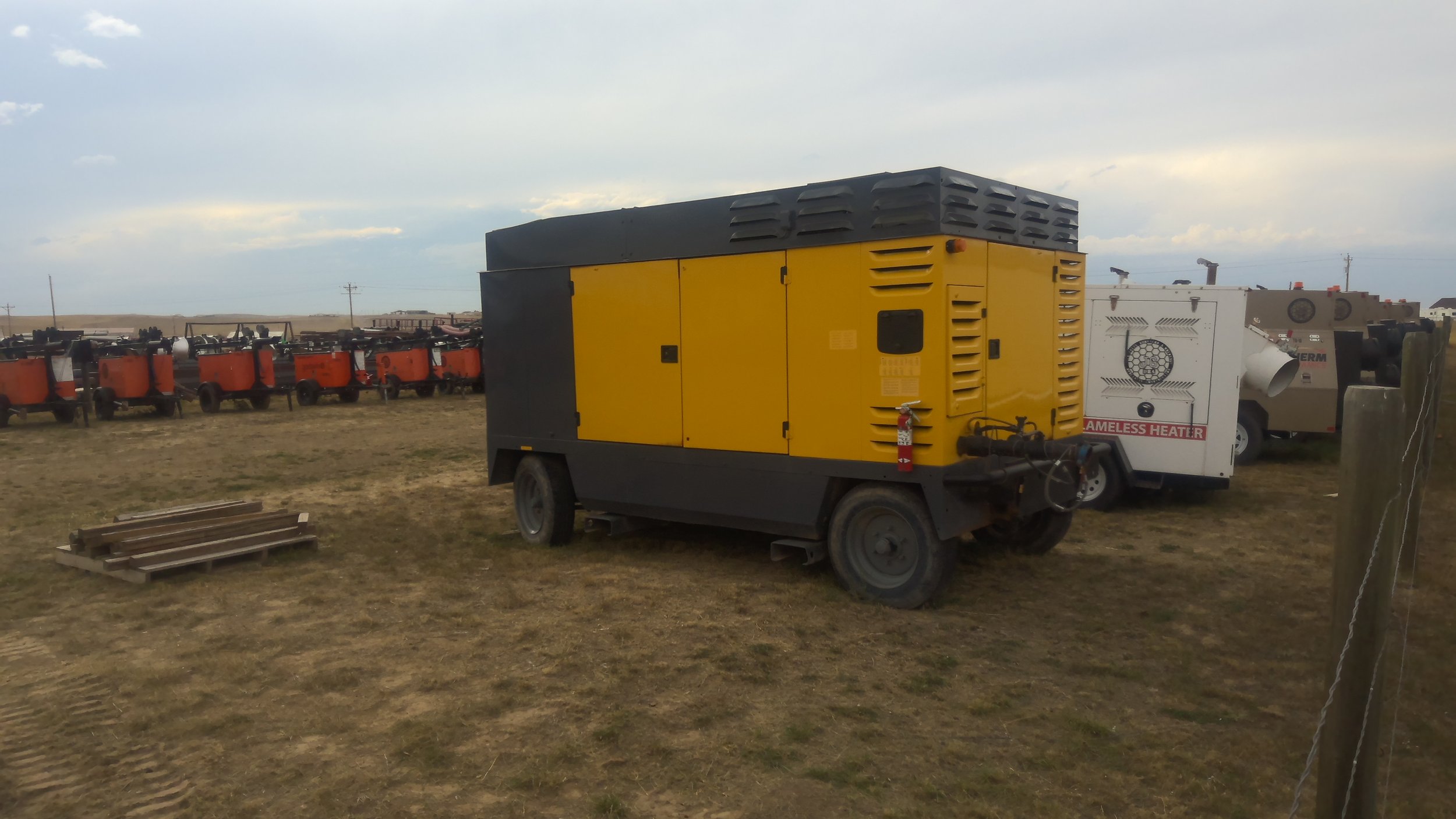 Yellow and black portable compressor on a grassy field with orange and white equipment in the background.