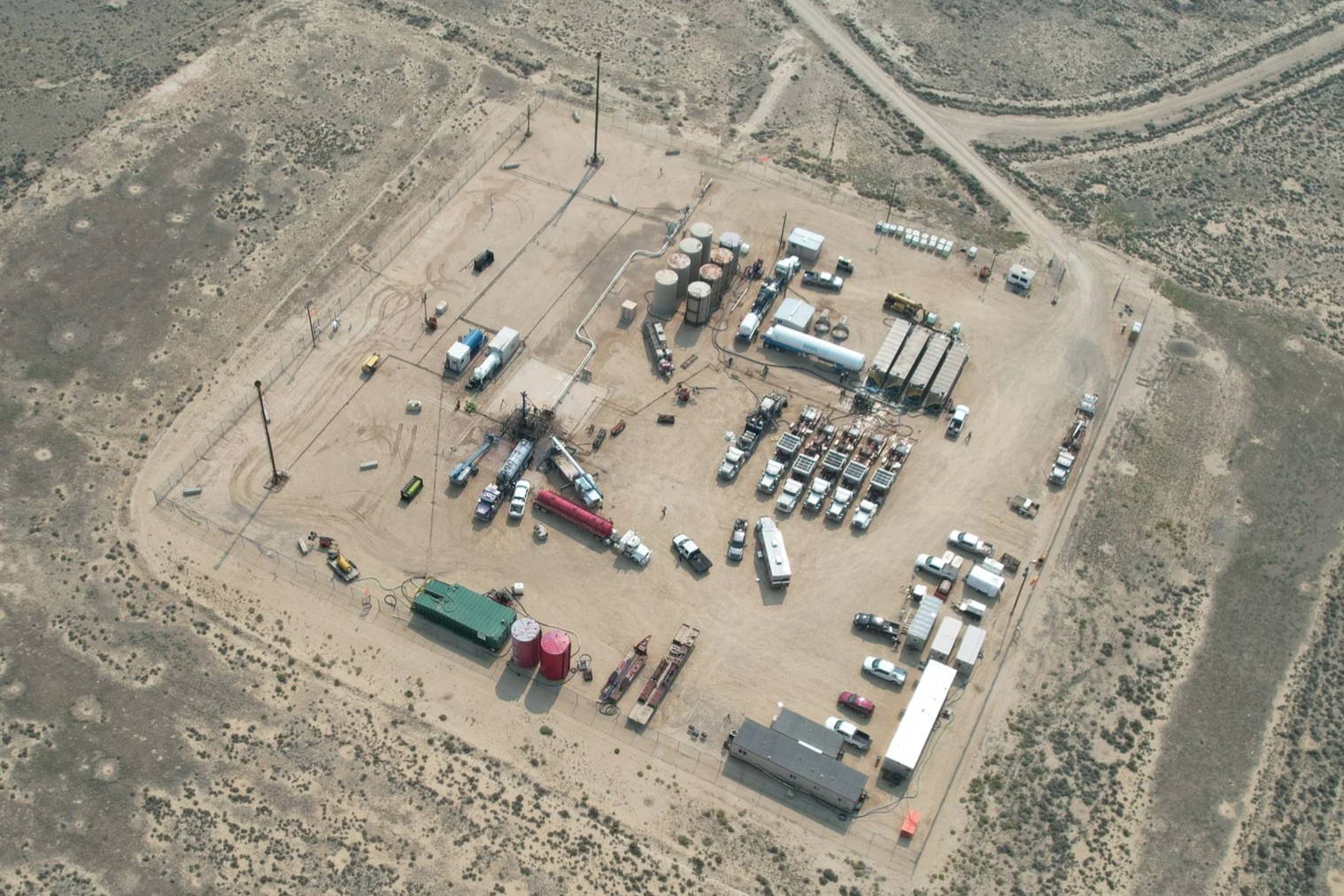 An aerial view of an industrial site with multiple trucks, tanks, and heavy machinery in a dry, desert landscape.