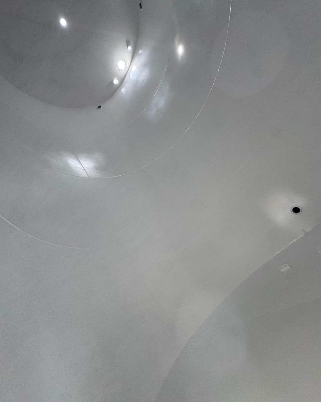 Close-up of a shiny, curved metallic ceiling with recessed lighting and small ventilation holes. epoxy coating after sand blasting
