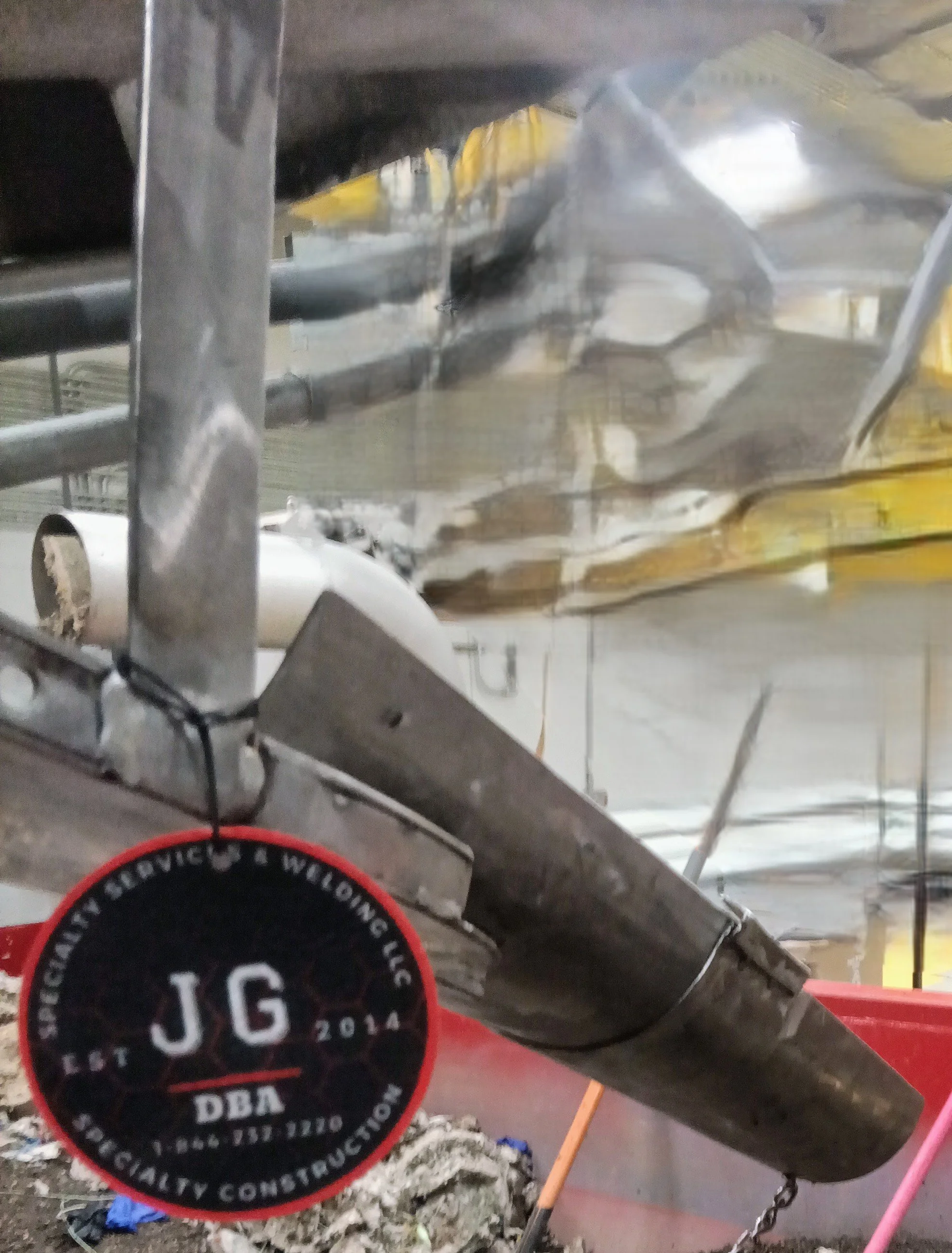 Close-up of a construction site with metal scaffolding, a black and red circular sticker reading 'J.G. 2014 DBA Specialty Construction,' and various construction materials and tools. custom made aluminum slider