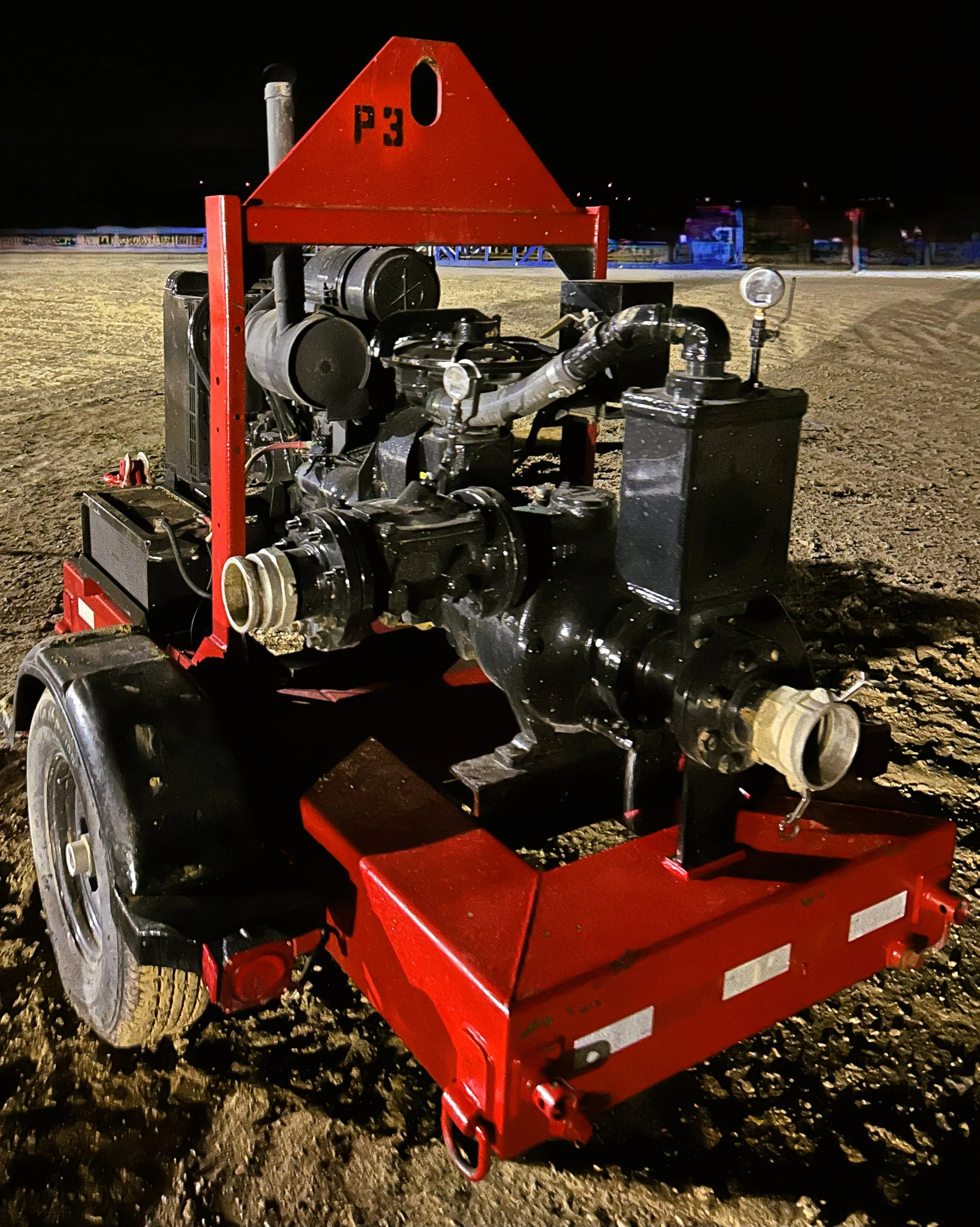 A portable, black fire pump with wheels on a dirt surface at night.