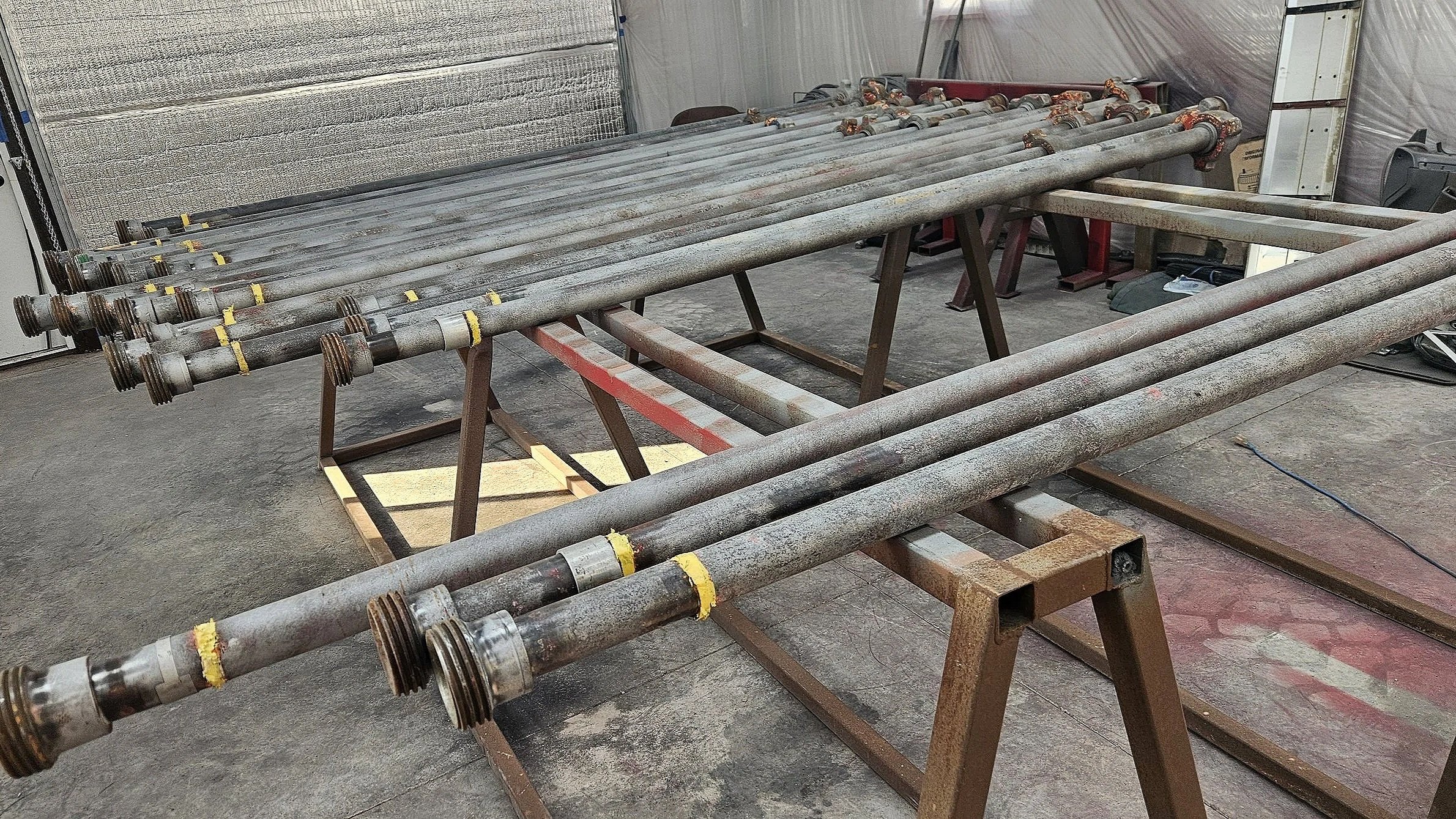 A workspace with multiple metal pipes laid out on wooden sawhorses in an indoor workshop or garage.